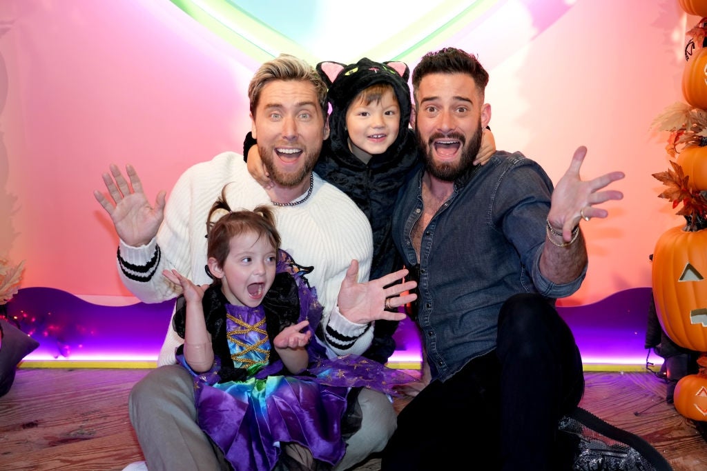 Two adults and two children in Halloween costumes smile and pose playfully at a festive event with pumpkins in the background
