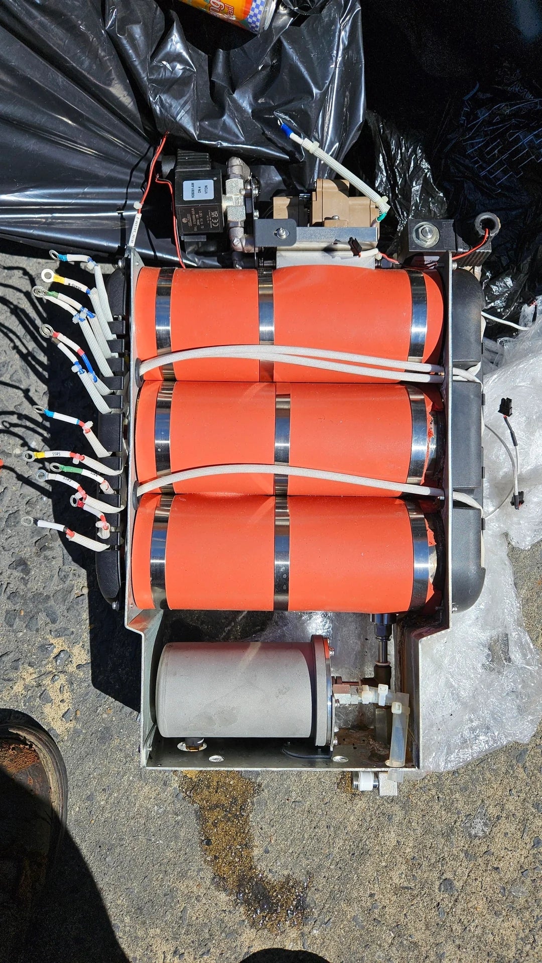 Device with orange cylinders and connected wires, possibly an electrical or mechanical component on a surface, with various parts visible