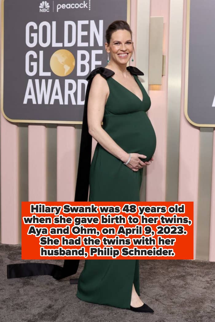 Person on red carpet in elegant gown holding baby bump, smiling at camera