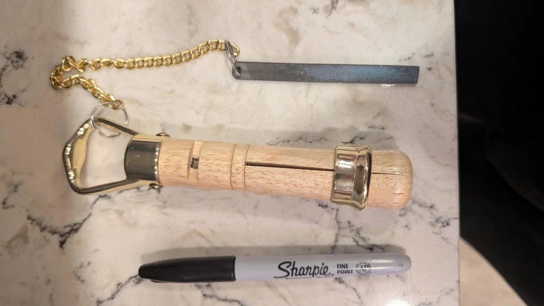 Wooden and metal nutcracker with a chain and blade beside a black Sharpie on a marble surface