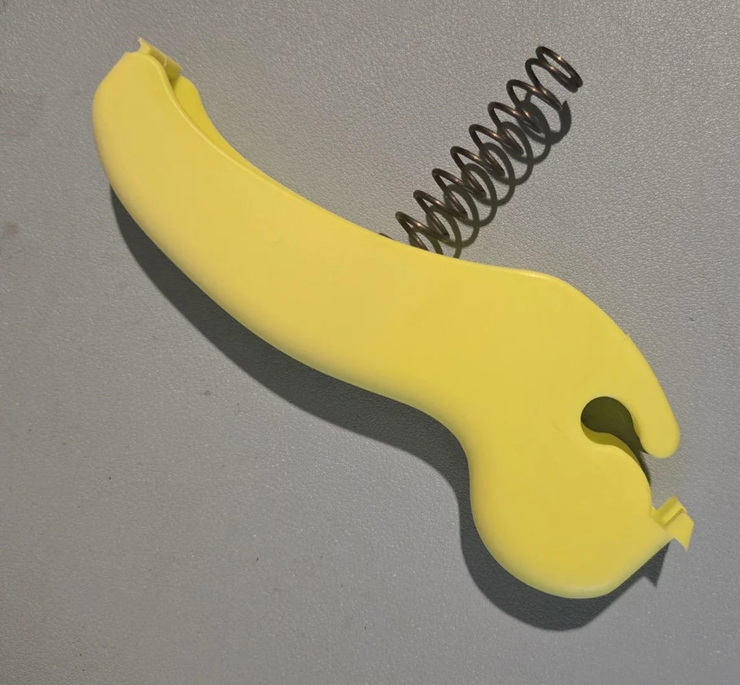 Yellow plastic banana slicer with a metal spring, laying on a gray surface
