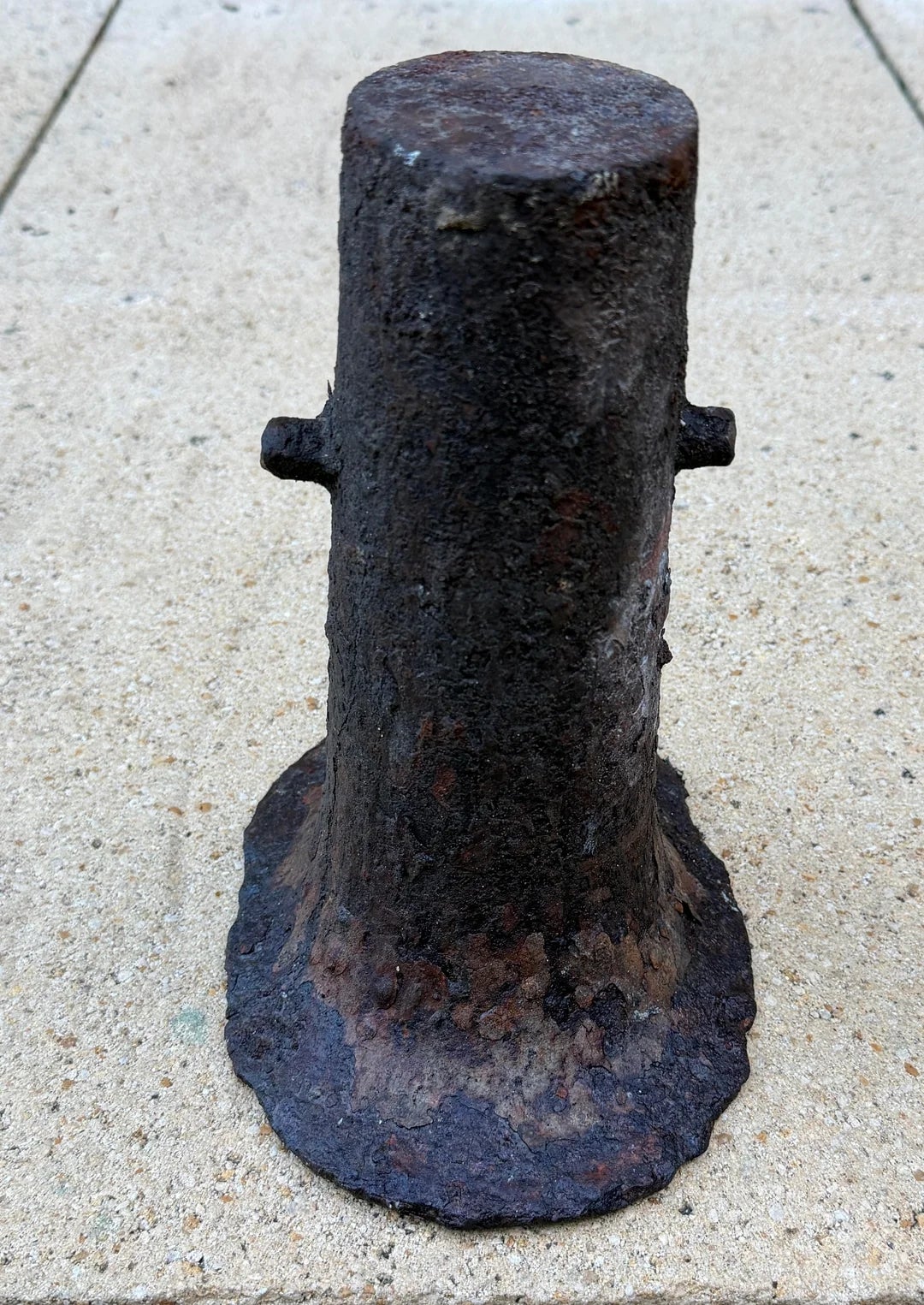 Rusty, cylindrical metal object on a textured surface, possibly an antique or industrial artifact