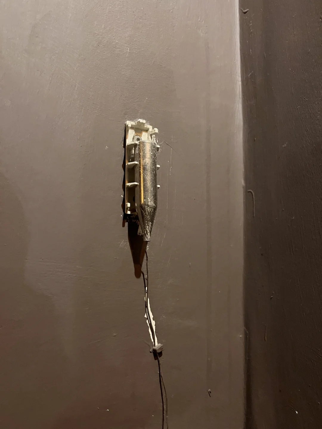 A broken and exposed light switch on a wall, showing wires protruding