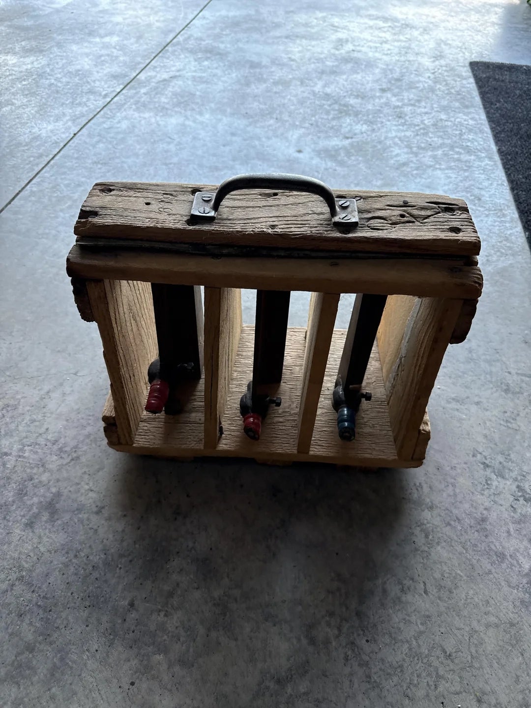 Wooden wine rack holding four bottles, viewed from above. The rack has a handle, giving it a rustic, handmade appearance