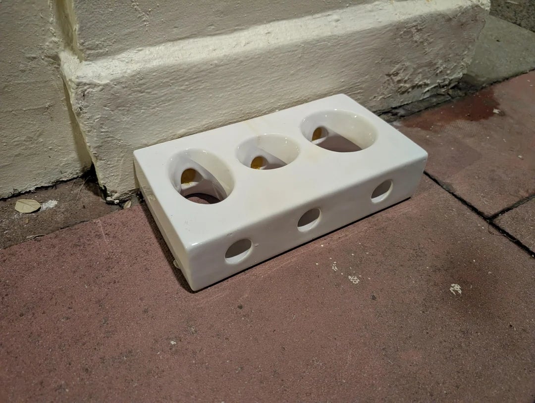 Ceramic brick designed as cheese with holes, leaning against a wall