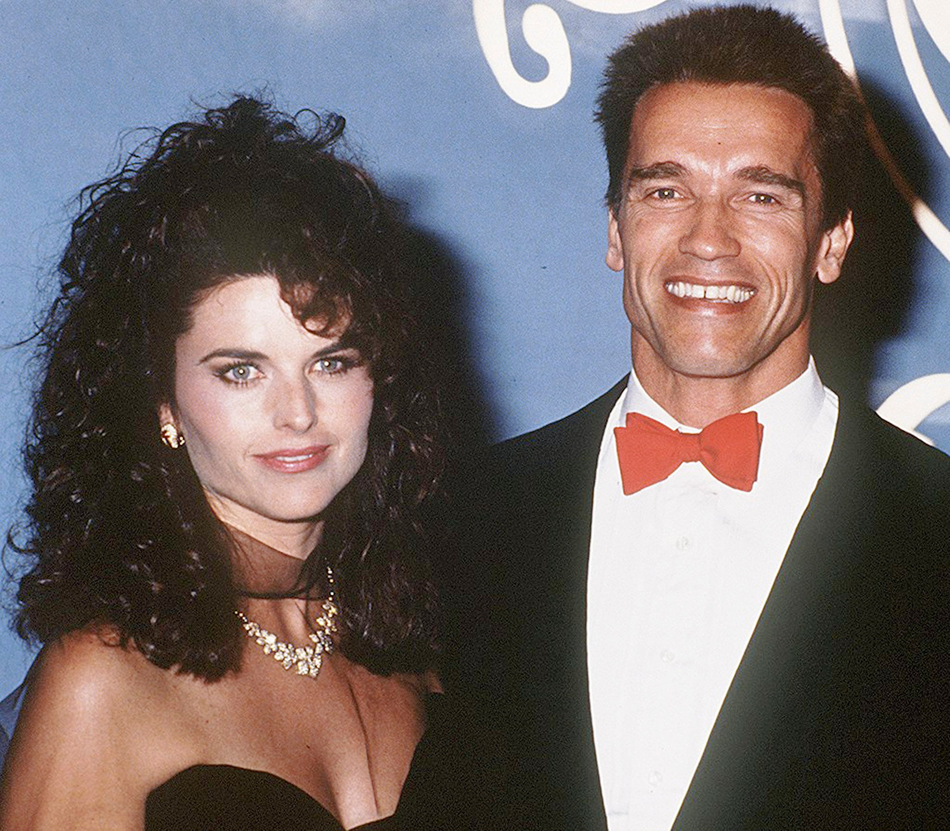 Maria Shriver and Arnold Schwarzenegger pose together. Shriver wears a black dress with a necklace, the Schwarzenegger wears a tuxedo and bow tie