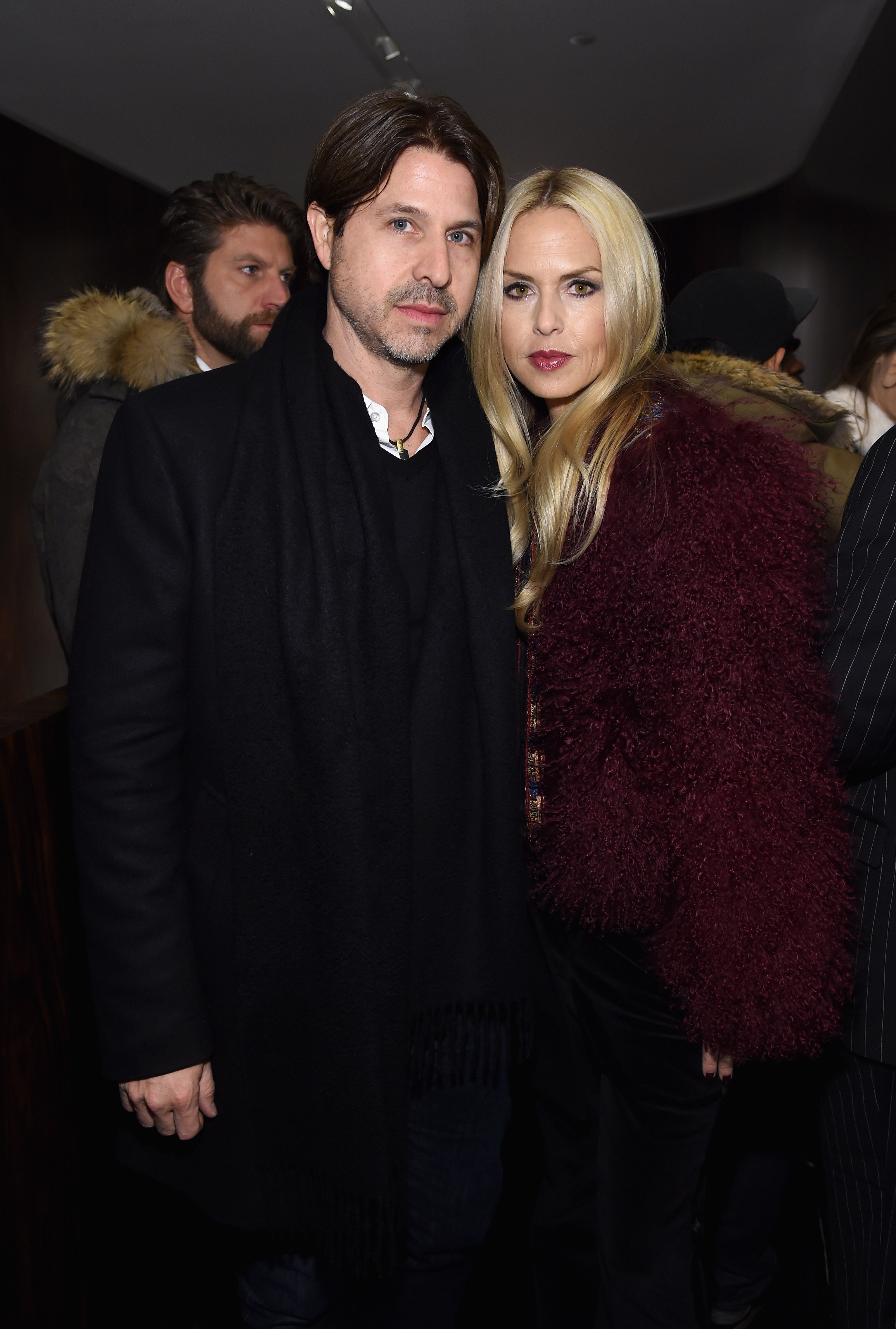 Rodger Berman and Rachel Zoe pose at an indoor event. Berman wears a dark jacket and Zoe wears a burgundy coat