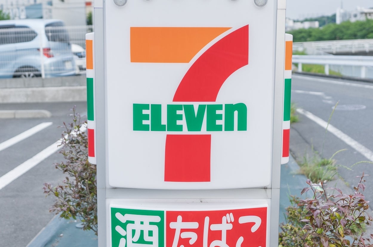 セブンイレブンの看板が駐車場に設置されている様子。酒、たばこ、銀行ATMのサービスを案内。