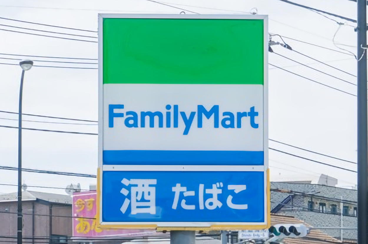 ファミリーマートの看板。下部に「酒」「たばこ」と書かれた青い文字。電柱や建物が背景に見える。