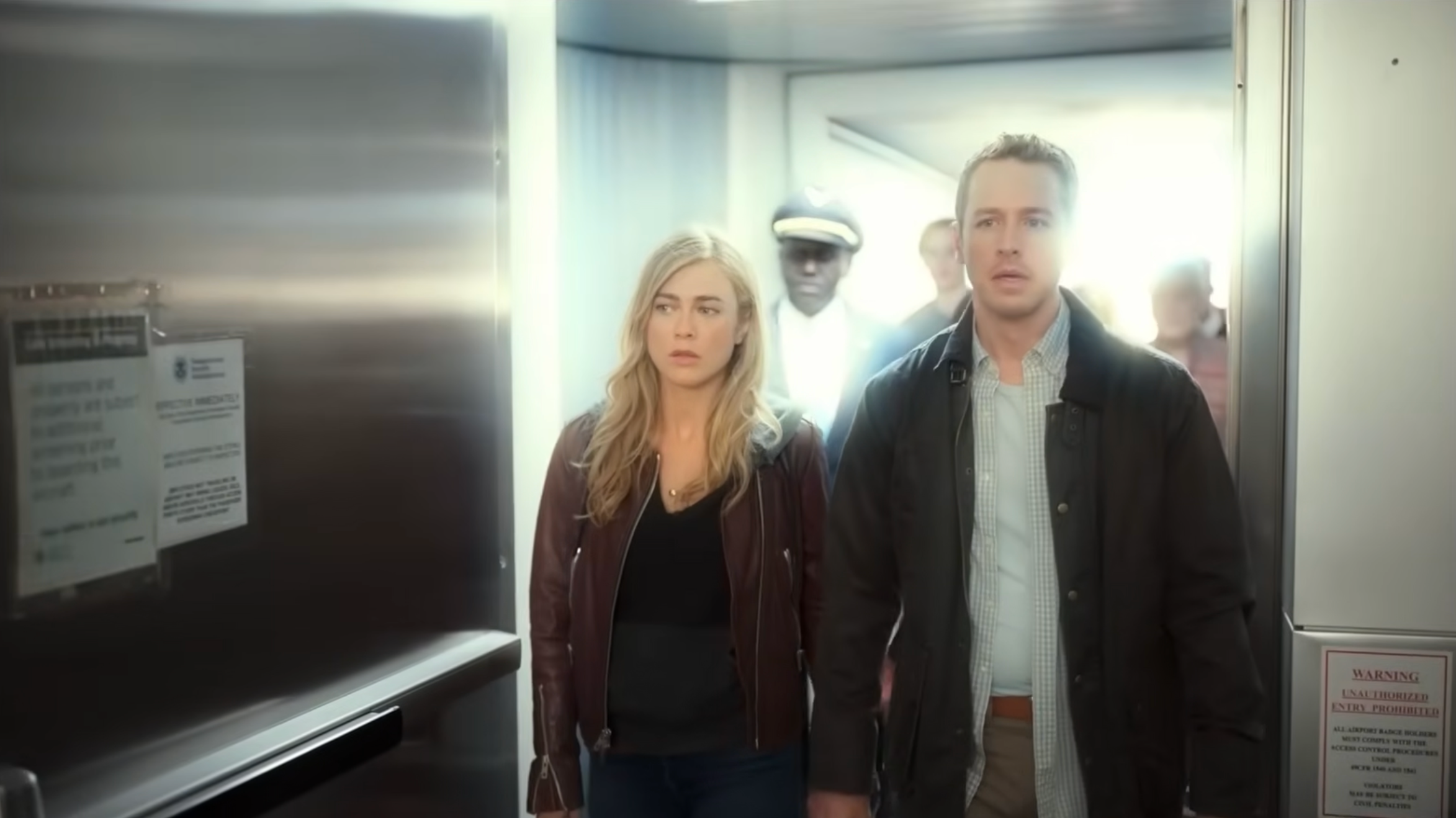 People walking purposefully in a corridor with serious expressions, possibly a scene from a movie or TV show