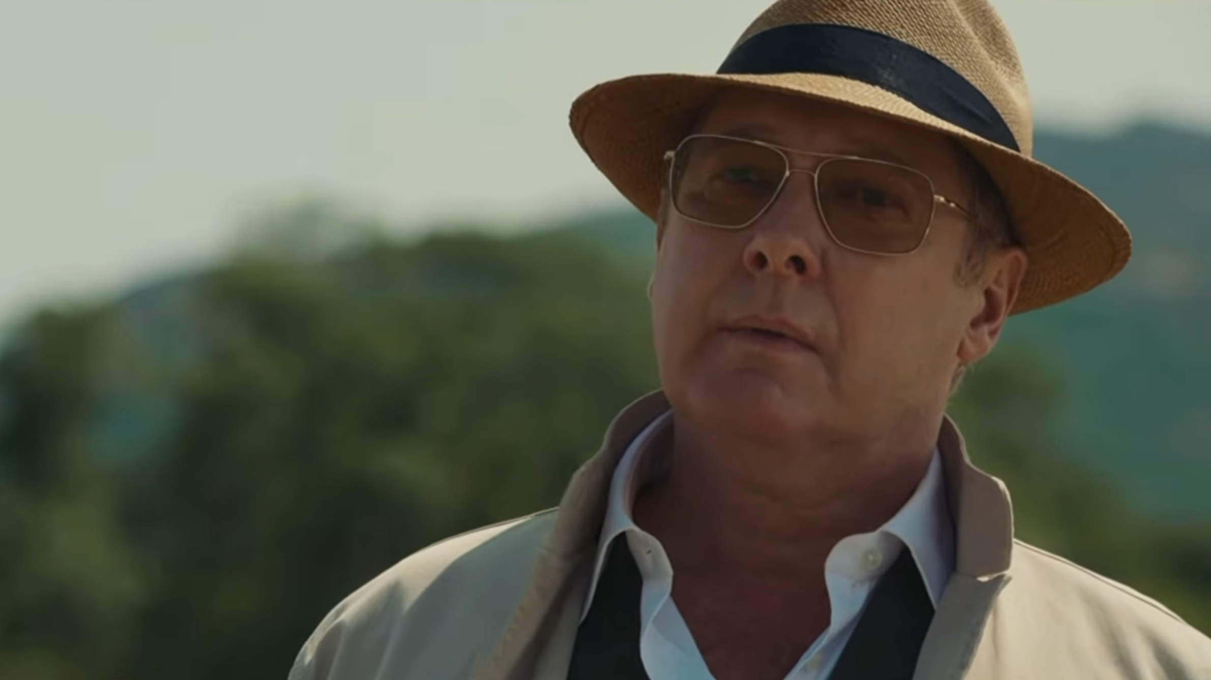 Person in a fedora and glasses, wearing a suit jacket, standing outdoors