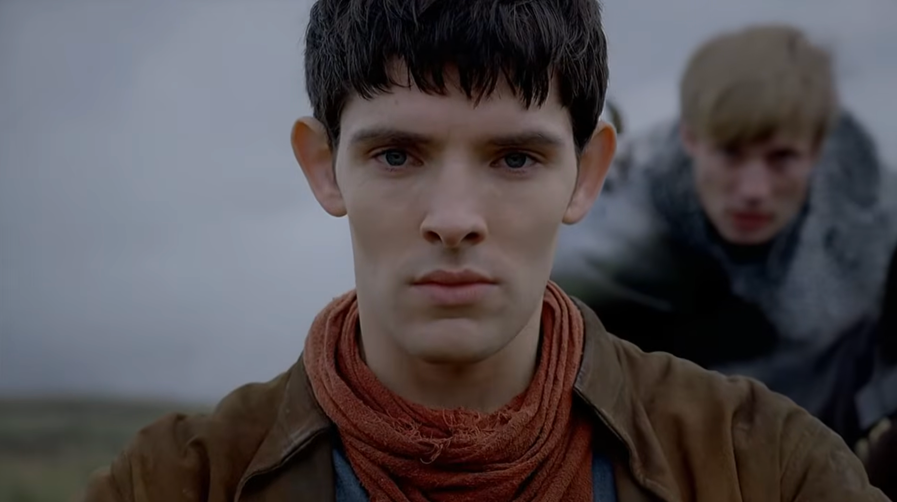 Two individuals in medieval attire outdoors, with one in focus at the front and the other slightly blurred in the background