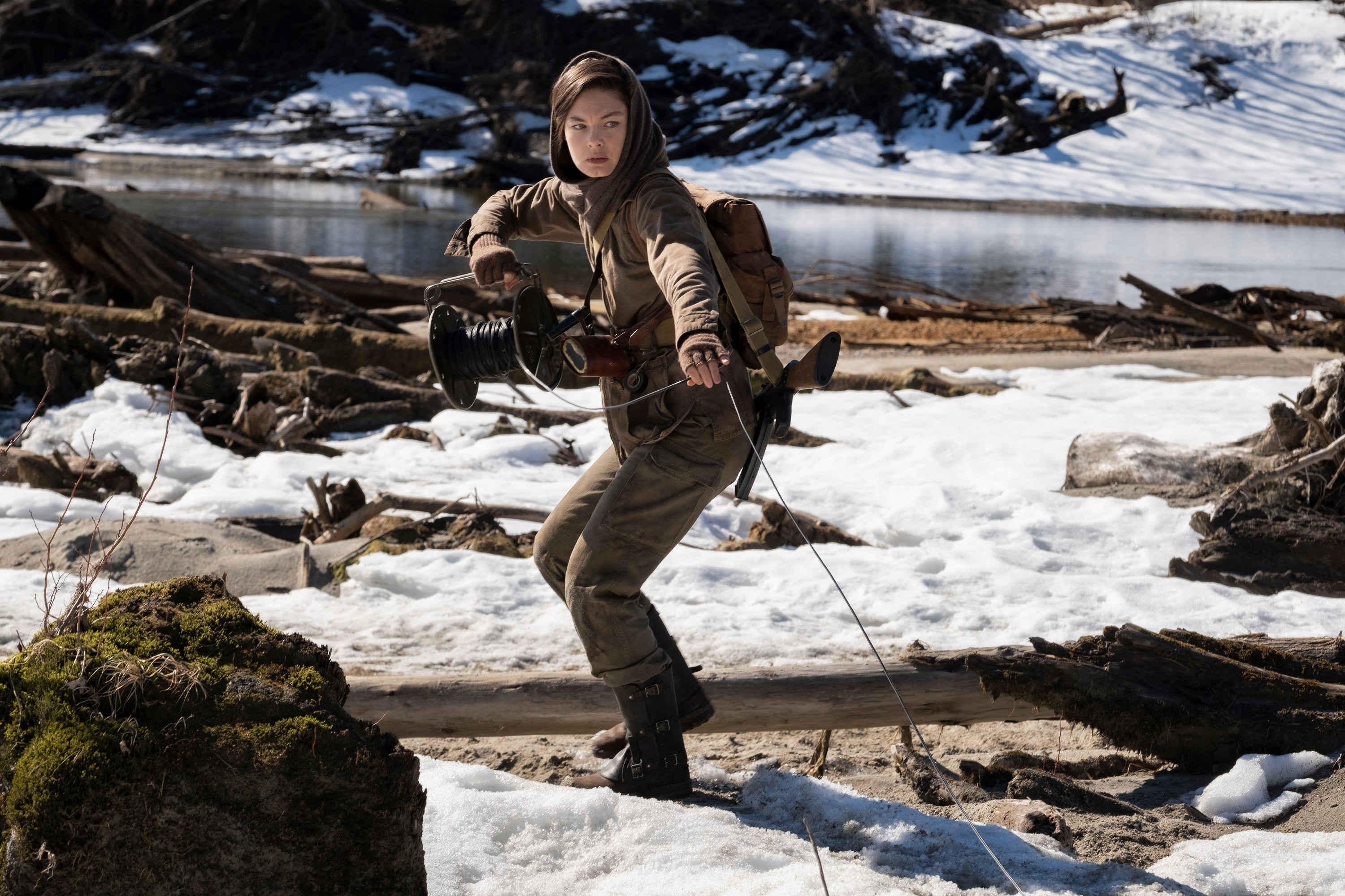 Person dressed in rugged outdoor attire, holding a wire, appears ready for action in a snowy, mountainous setting