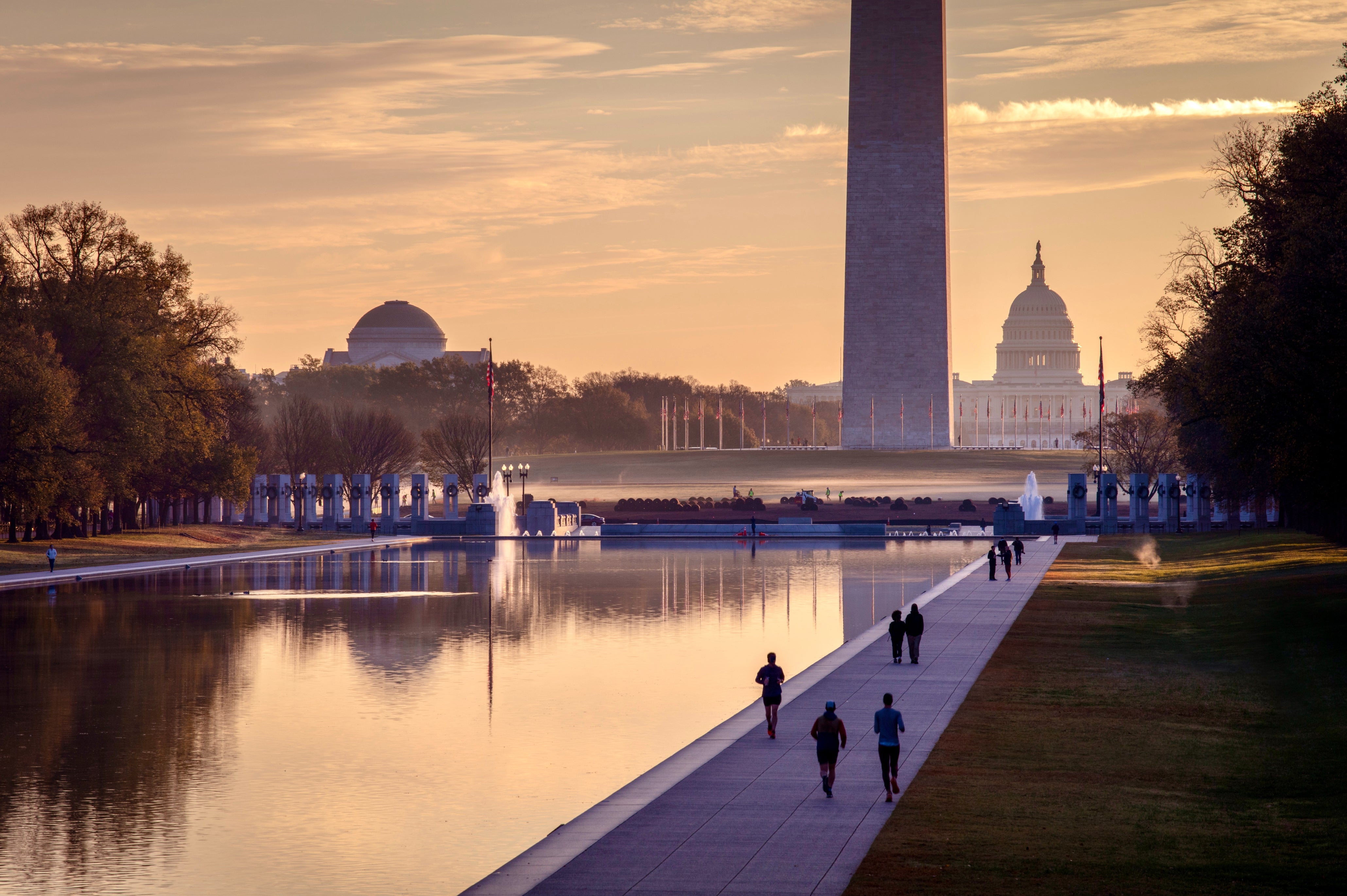 Folk går langs Reflecting Pool i Washington, DC, med Washington Monument og US Capitol i bakgrunnen ved soloppgang