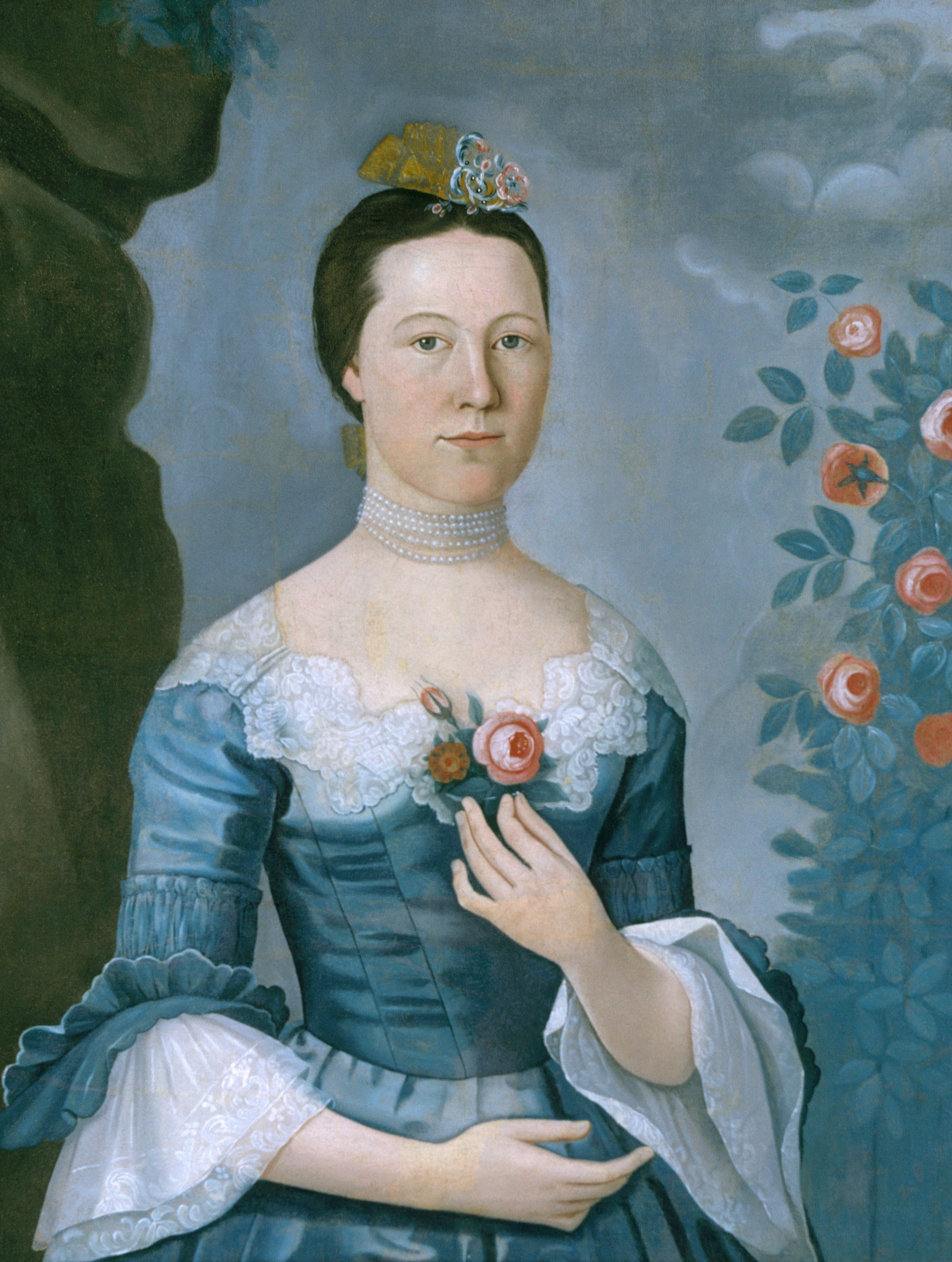 En kvinne i 1700-tallsdrakt står ved roser, ikledd en blondetrimmet kjole og perlechoker, og holder en blomst med balansert eleganse