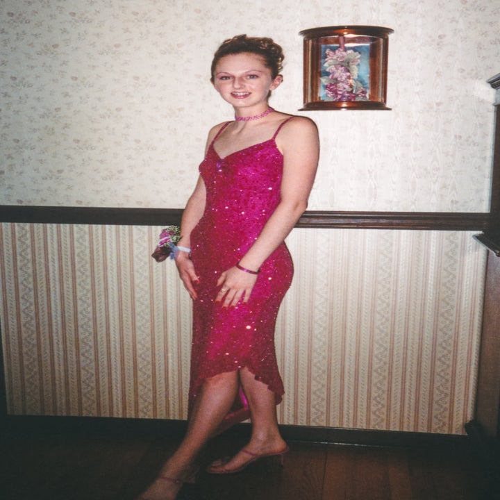 Person in a pink sequined dress standing in a room with patterned wallpaper, smiling