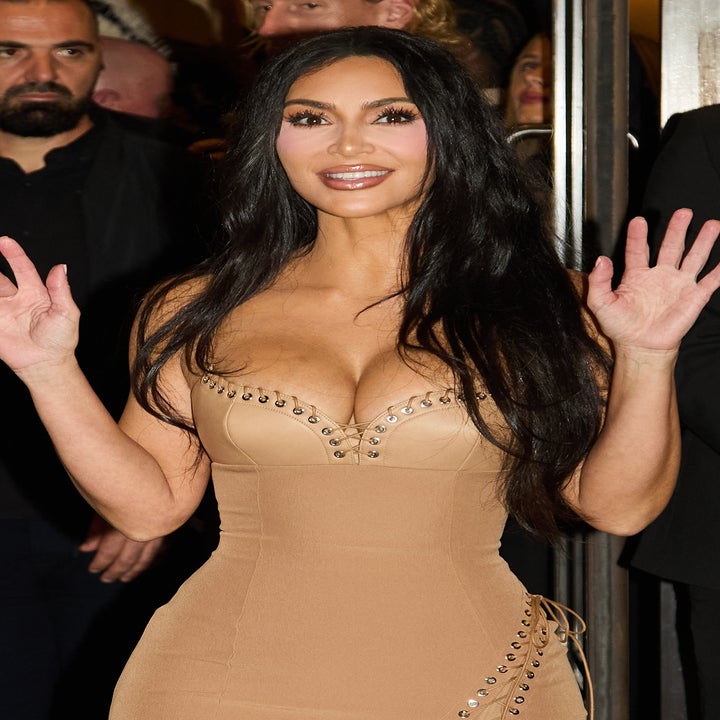 Person waving and smiling in a form-fitting dress adorned with sparkly embellishments