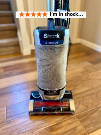 Shark Stratos vacuum cleaner connected a woody floor, showcasing its filled dustbin for a location cleaning article