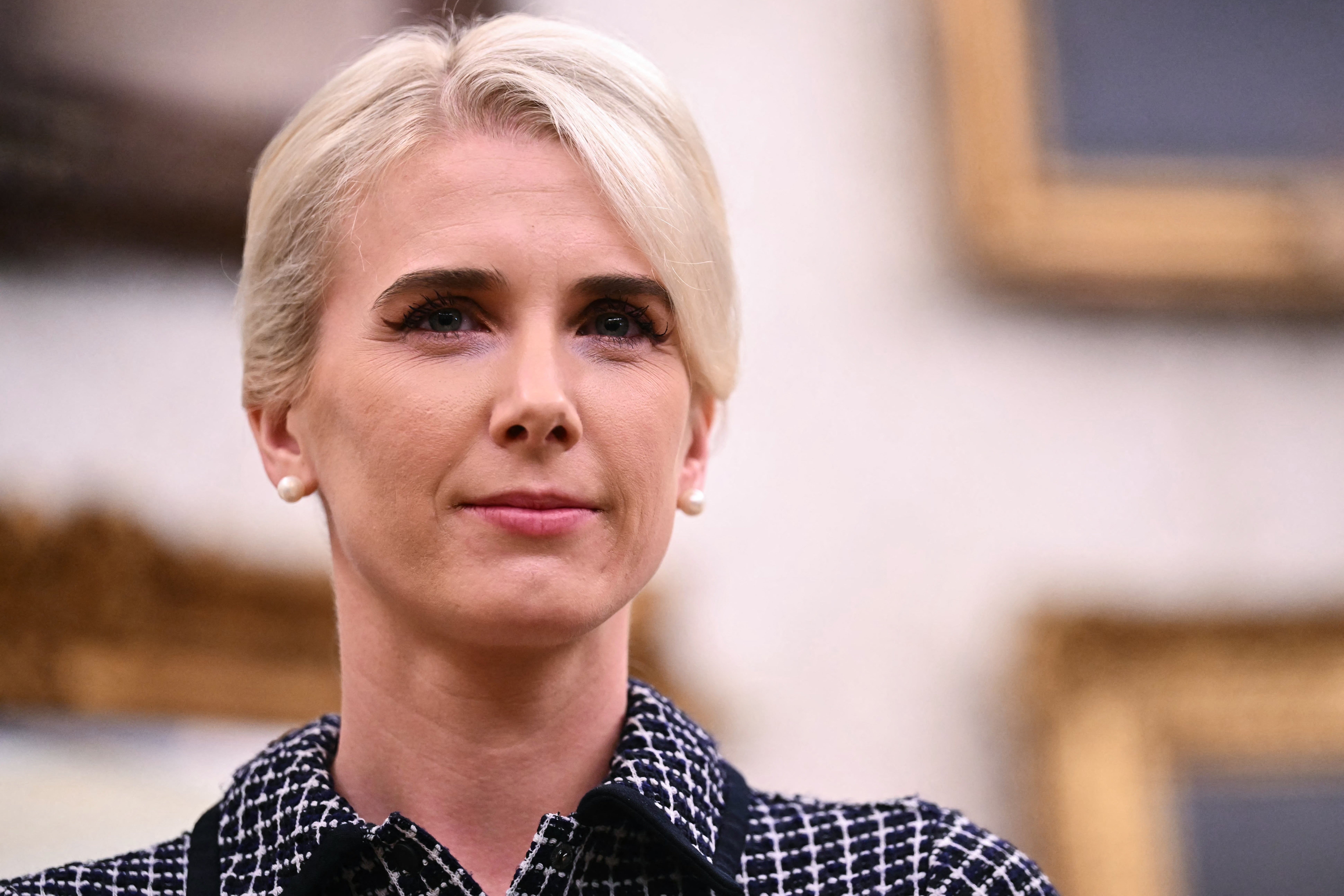 Person med kort, stylet hår i rutete antrekk, stående i en formell setting