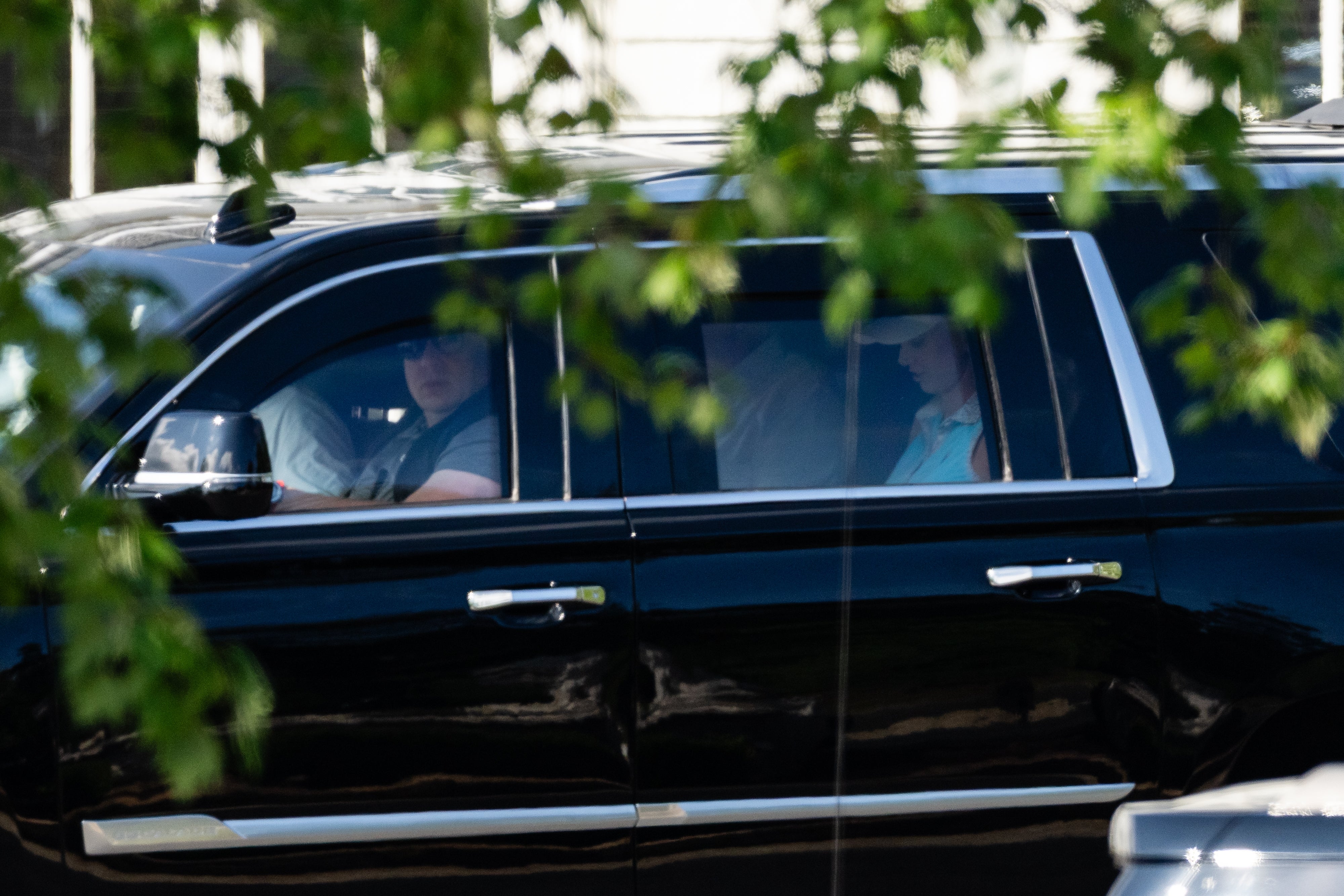 En person sitter bak på en svart SUV, delvis skjult av løvverk