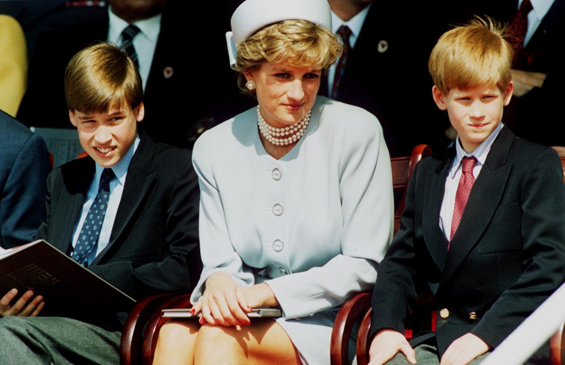 A woman in formal attire with two young boys, both in suits, sitting at an outdoor event