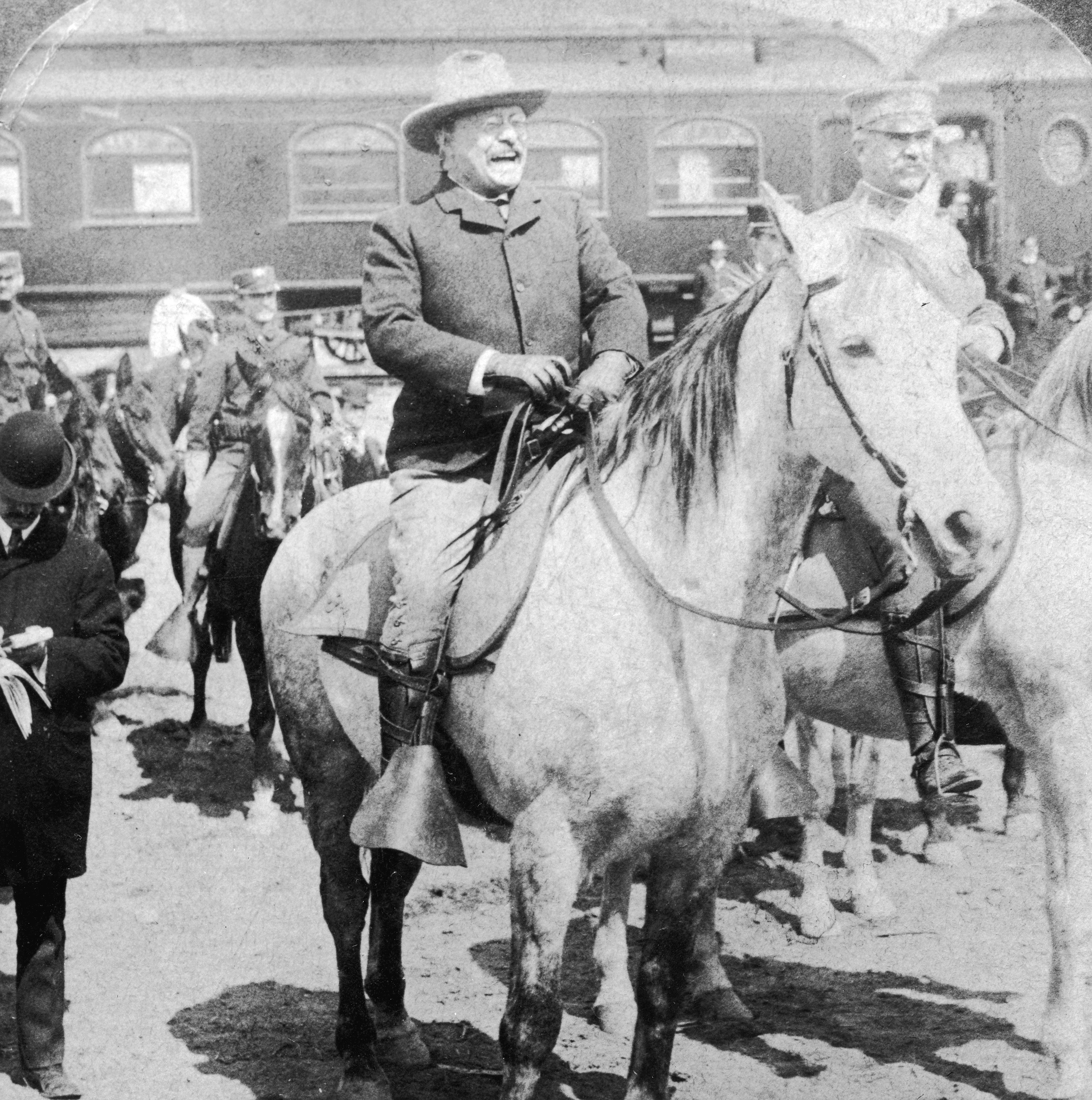 En historisk skikkelse på hesteryggen, omgitt av andre i lignende antrekk nær et tog, ser ut til å være en del av en offisiell begivenhet eller seremoni