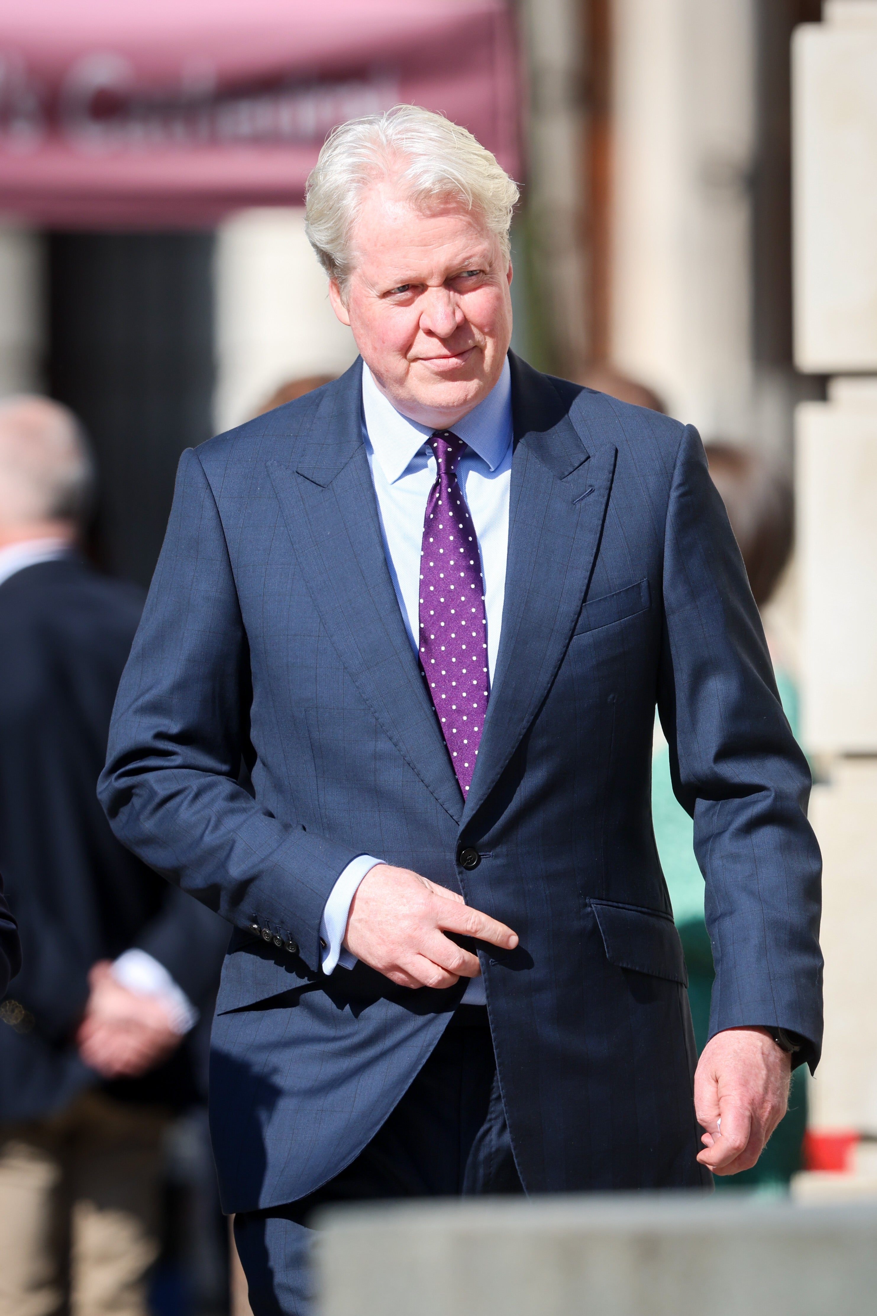 A person in a tailored suit and tie is walking outdoors, looking to the side