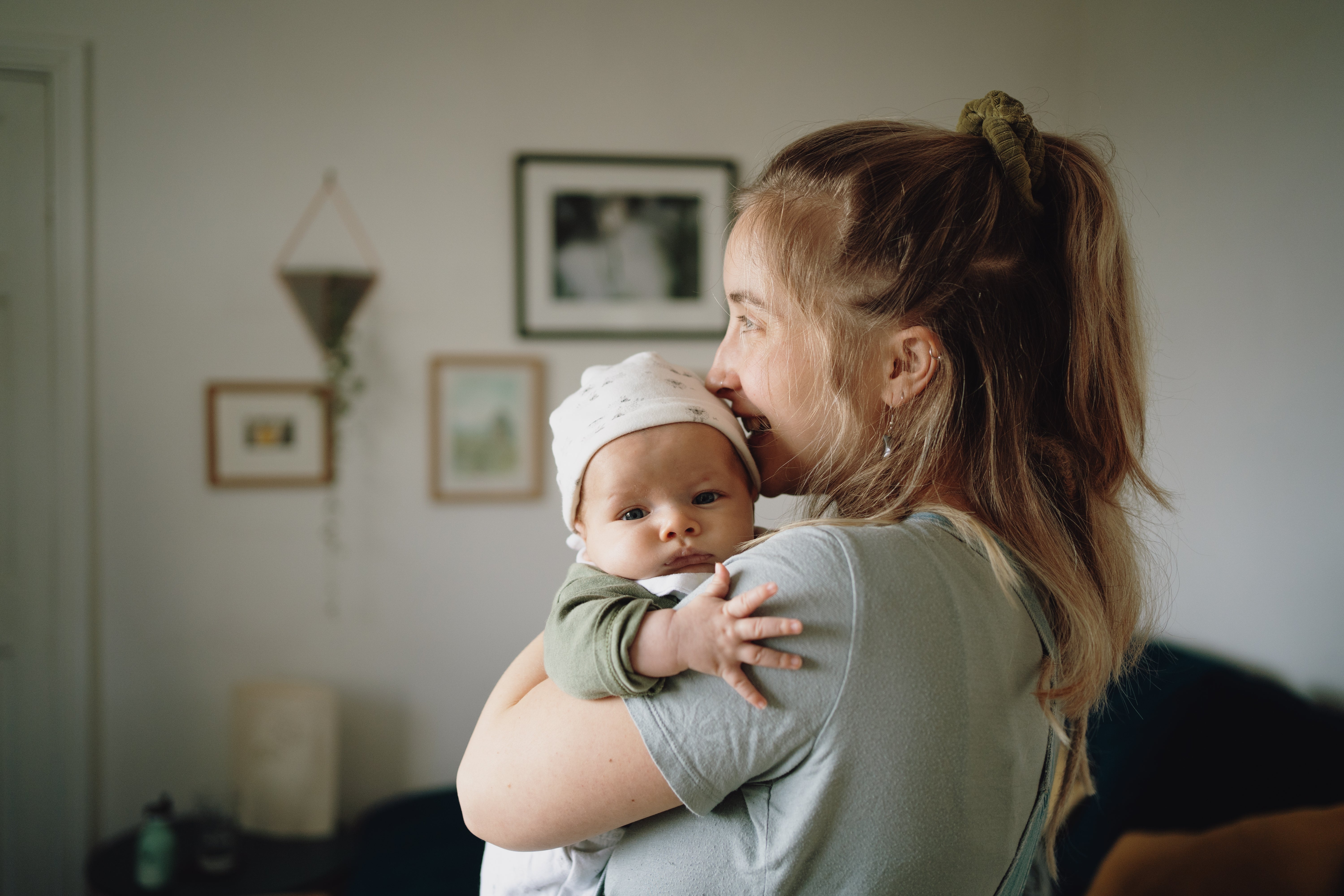 En kvinne som holder en baby i en koselig hjemmesetting, begge stirrer mot vinduet