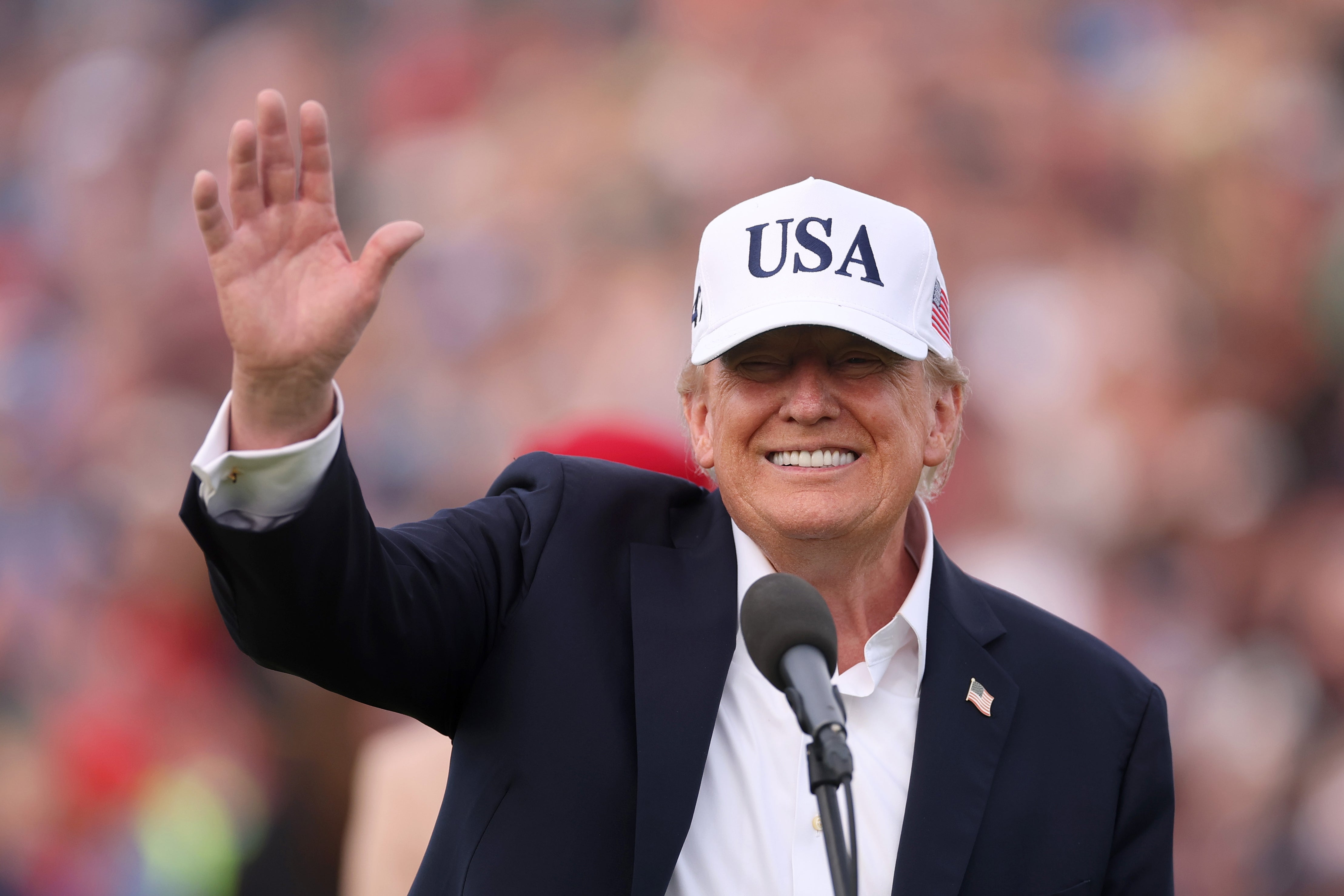 Jeg vet ikke hvem dette er, men personen har på seg en "USA" caps, vinke og stå foran en mikrofon på et utendørsarrangement