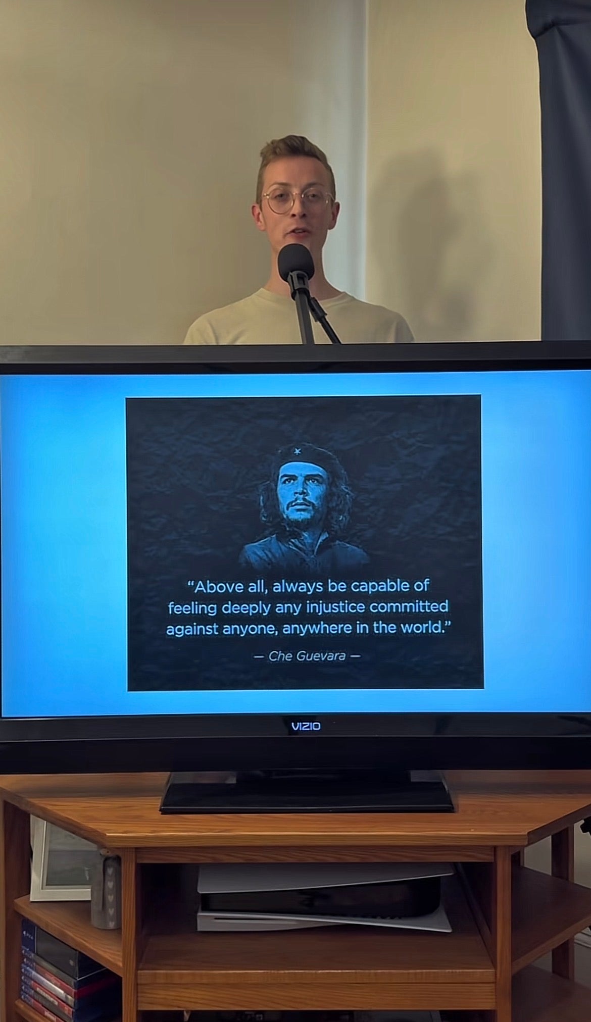 En person snakker inn i en mikrofon ved siden av en skjerm som viser et Che Guevara-sitat om empati og urettferdighet