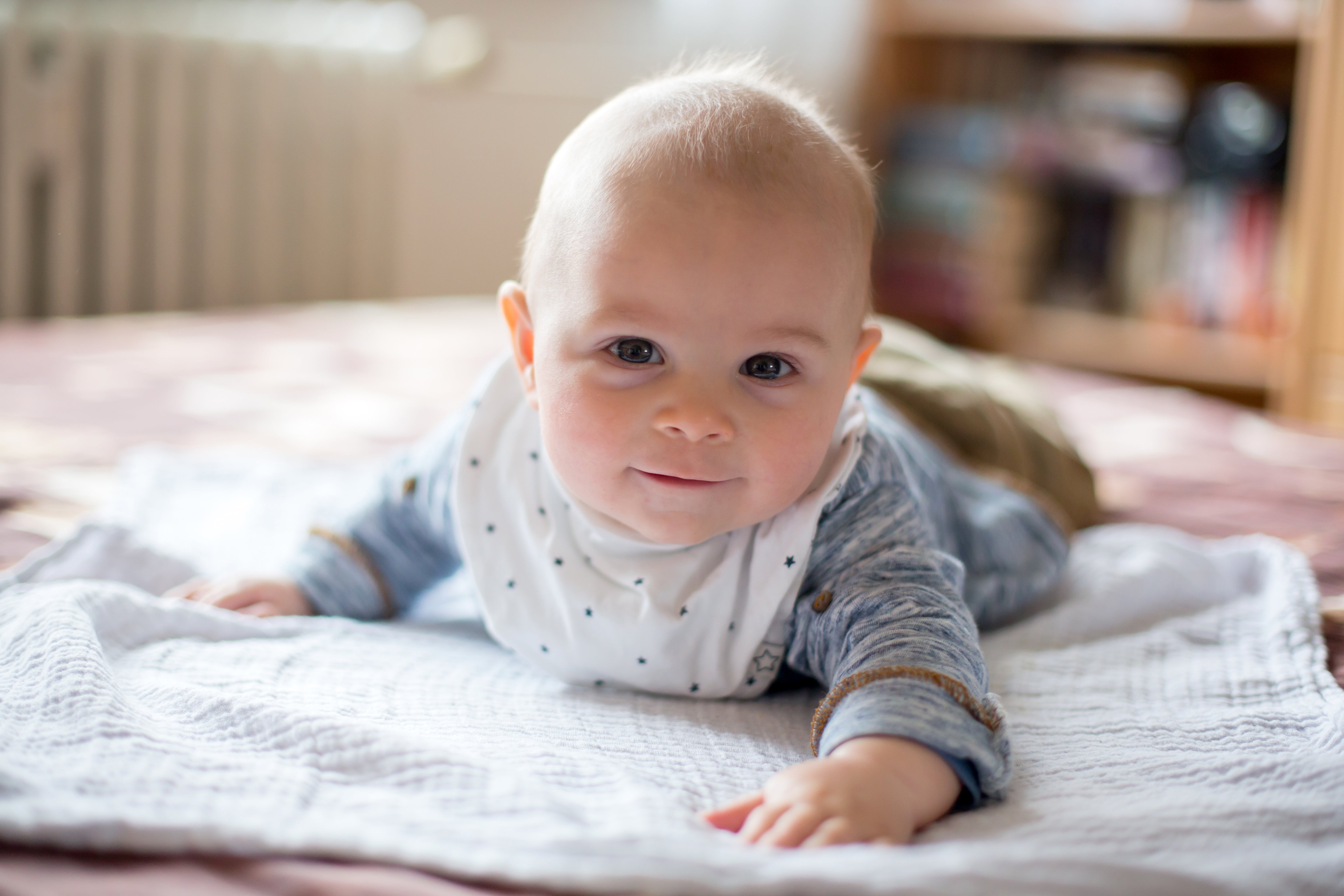Baby ligger på magen på et teppe og ser på kameraet med et nysgjerrig uttrykk