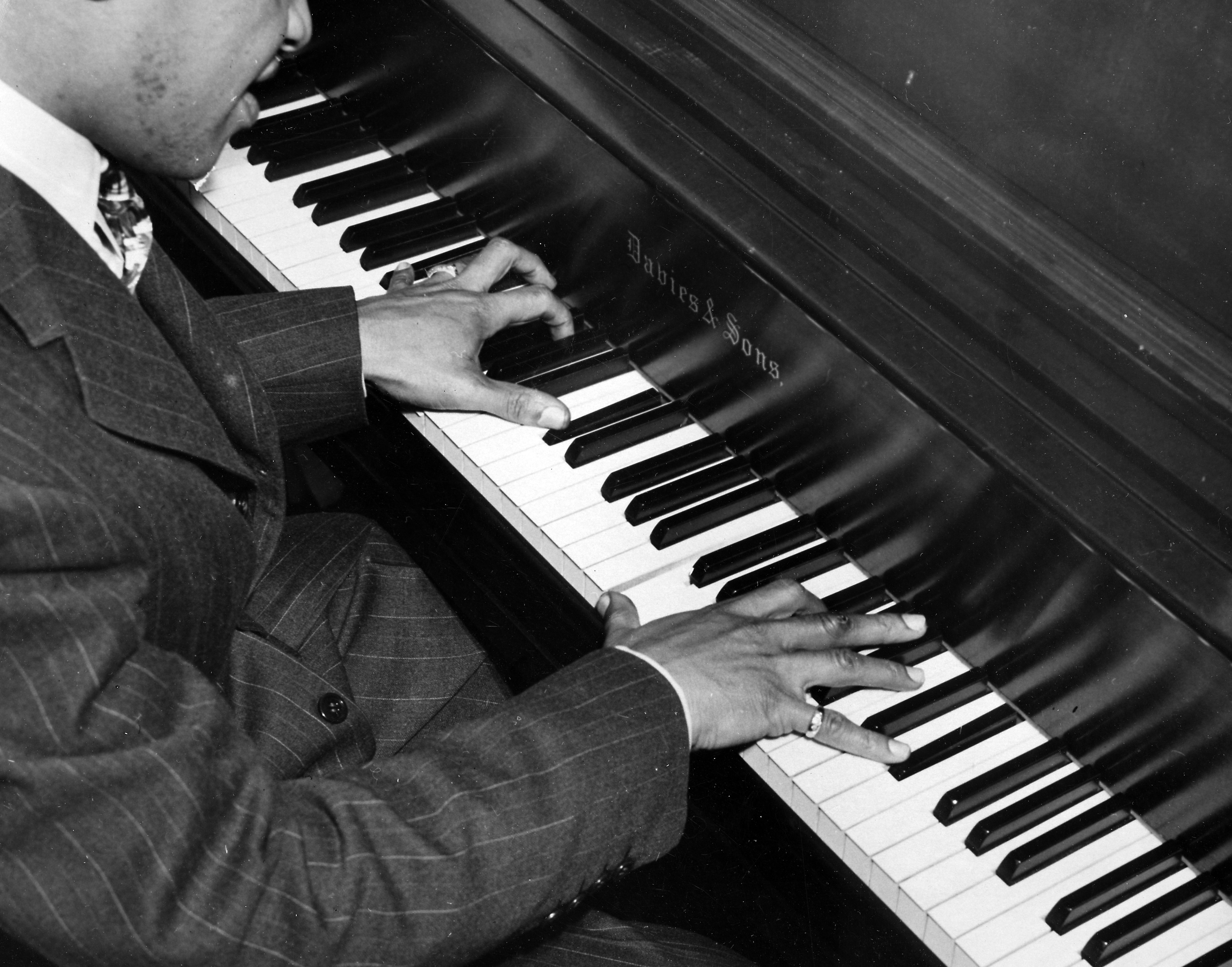 Person in a suit playing the piano with focused hands on the keys