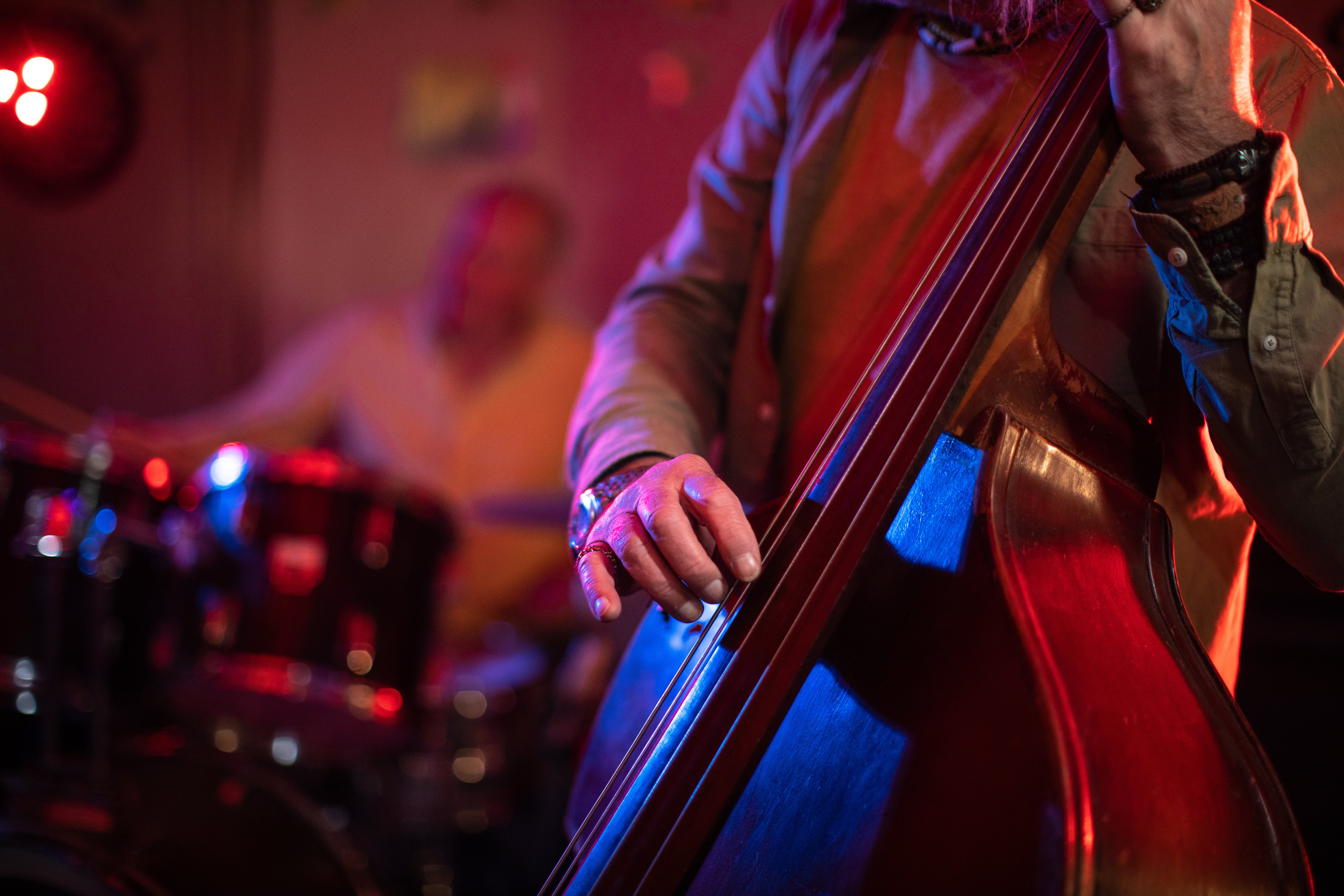Person playing a double bass with another musician on drums in the background, creating a lively musical ambiance