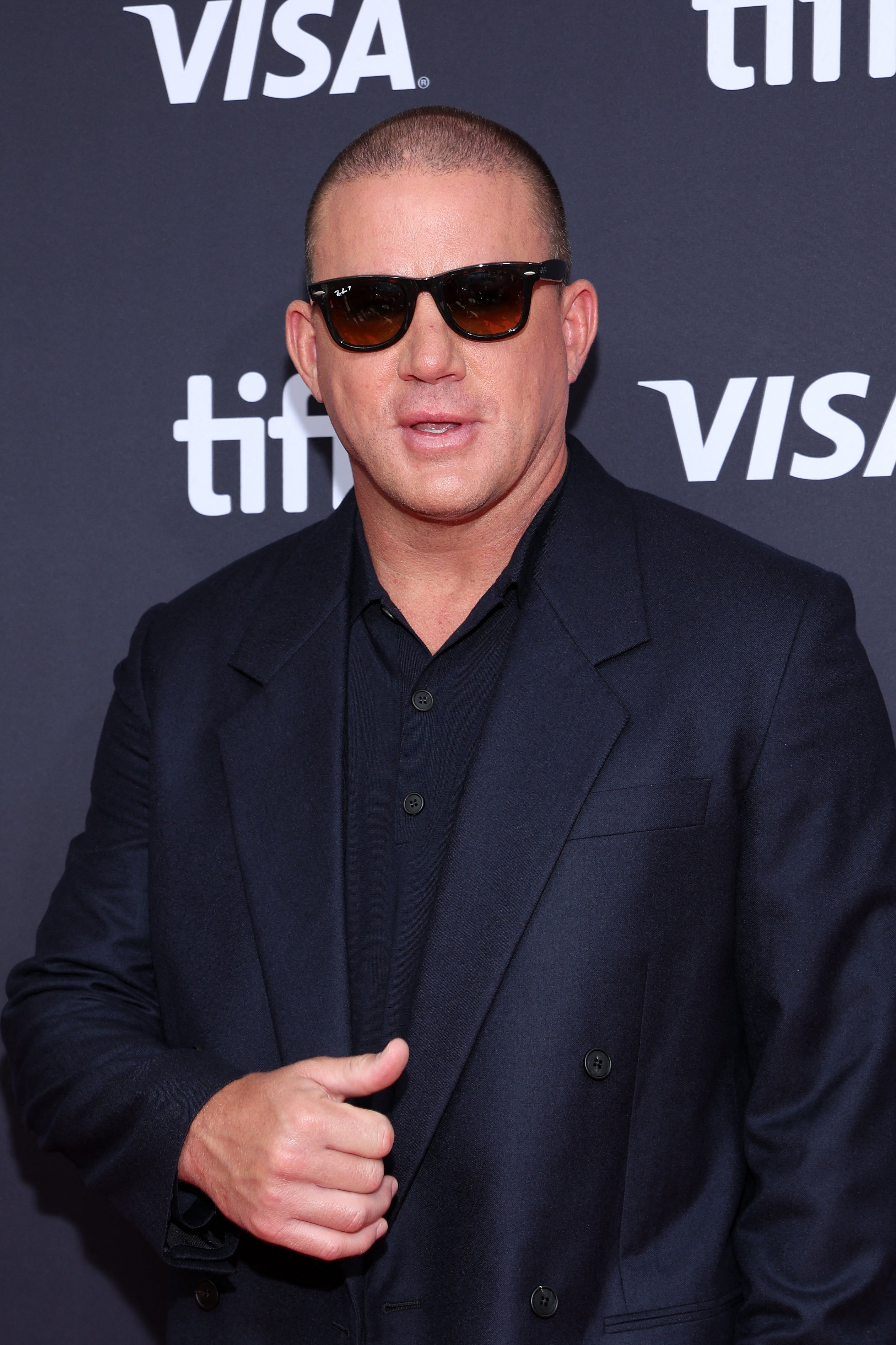 A person in sunglasses wearing a classic dark suit on the red carpet at a TIFF event