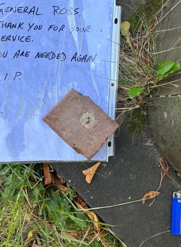Note on the ground reads: “General Ross thank you for your service. You are needed again. R.I.P.” A blue lighter and stone are nearby