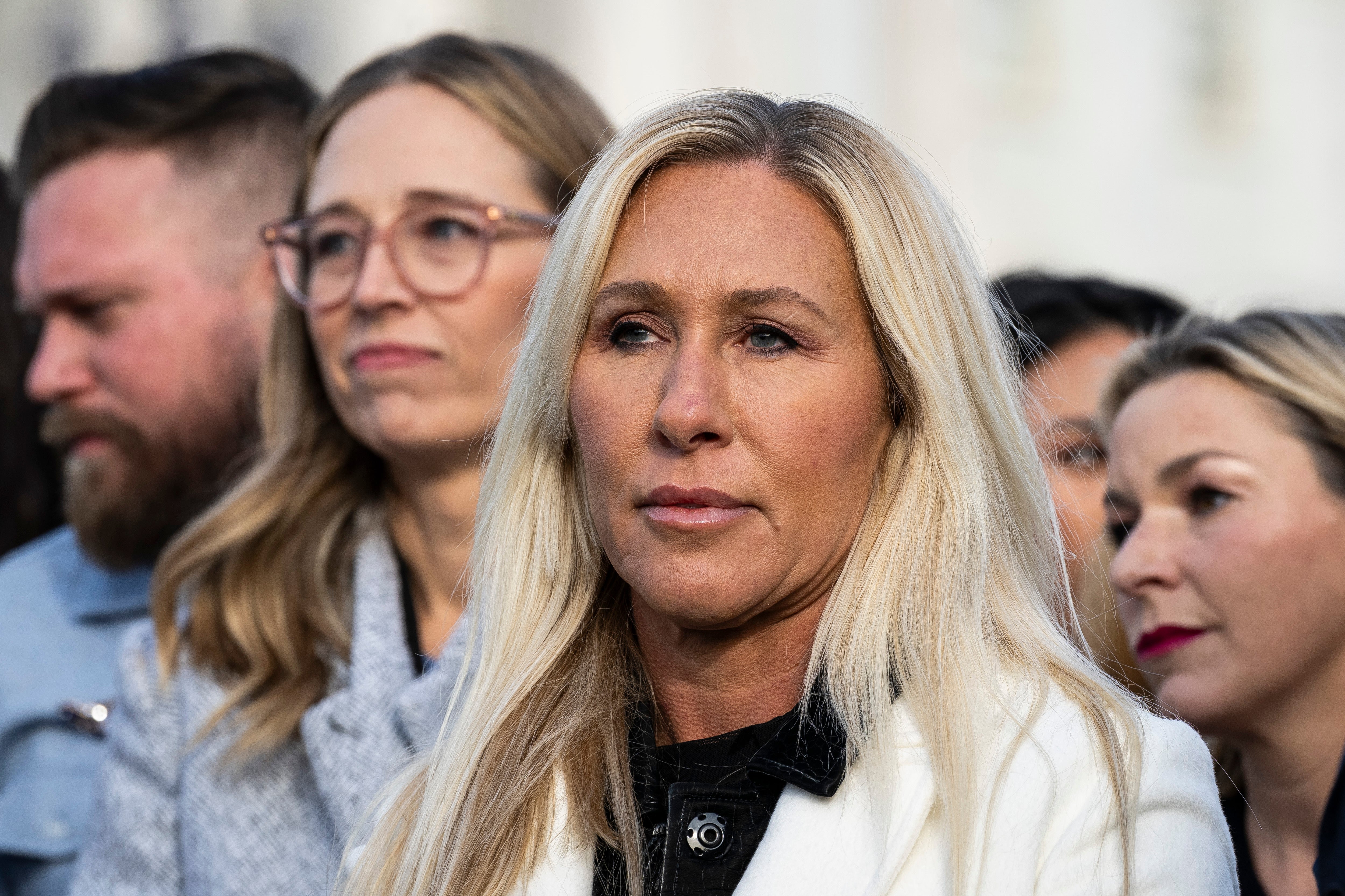 Gruppe individer, inkludert en kvinne i fokus iført en hvit blazer, står utenfor