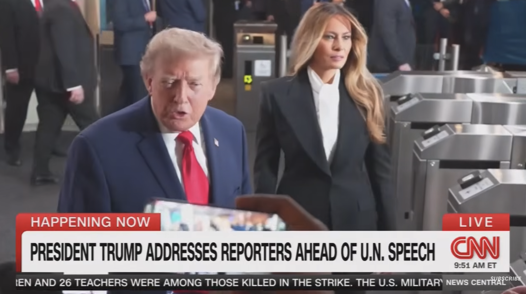 En mann i dress snakker med journalister med en kvinne i blazer ved siden av seg på et travelt sted. Et CNN-nyhetsbanner er synlig