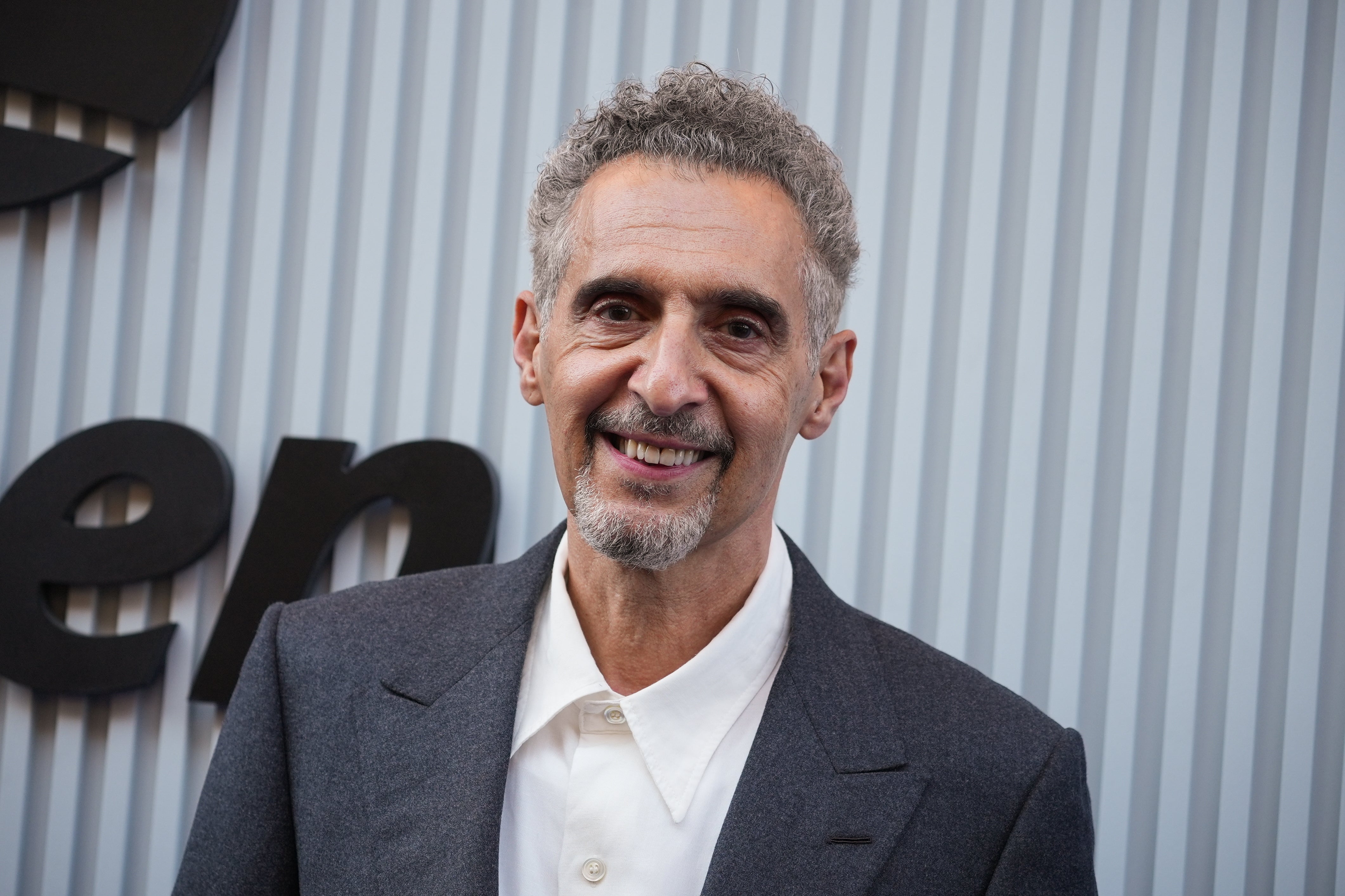 A person in a smart suit smiles in front of a backdrop with text