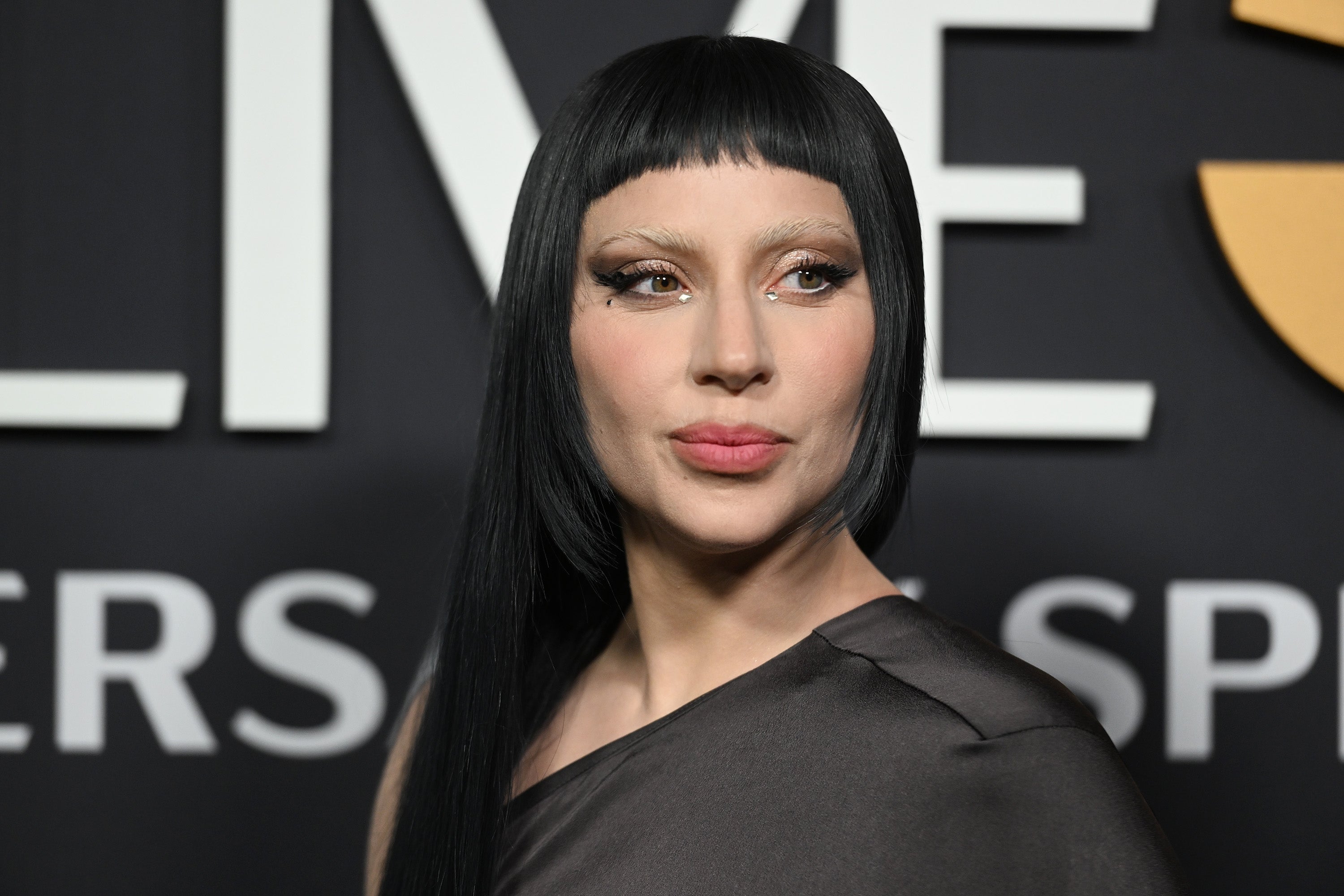 Person with straight, dark hair and unique eyeliner wearing a fashionable, asymmetrical top at a formal event