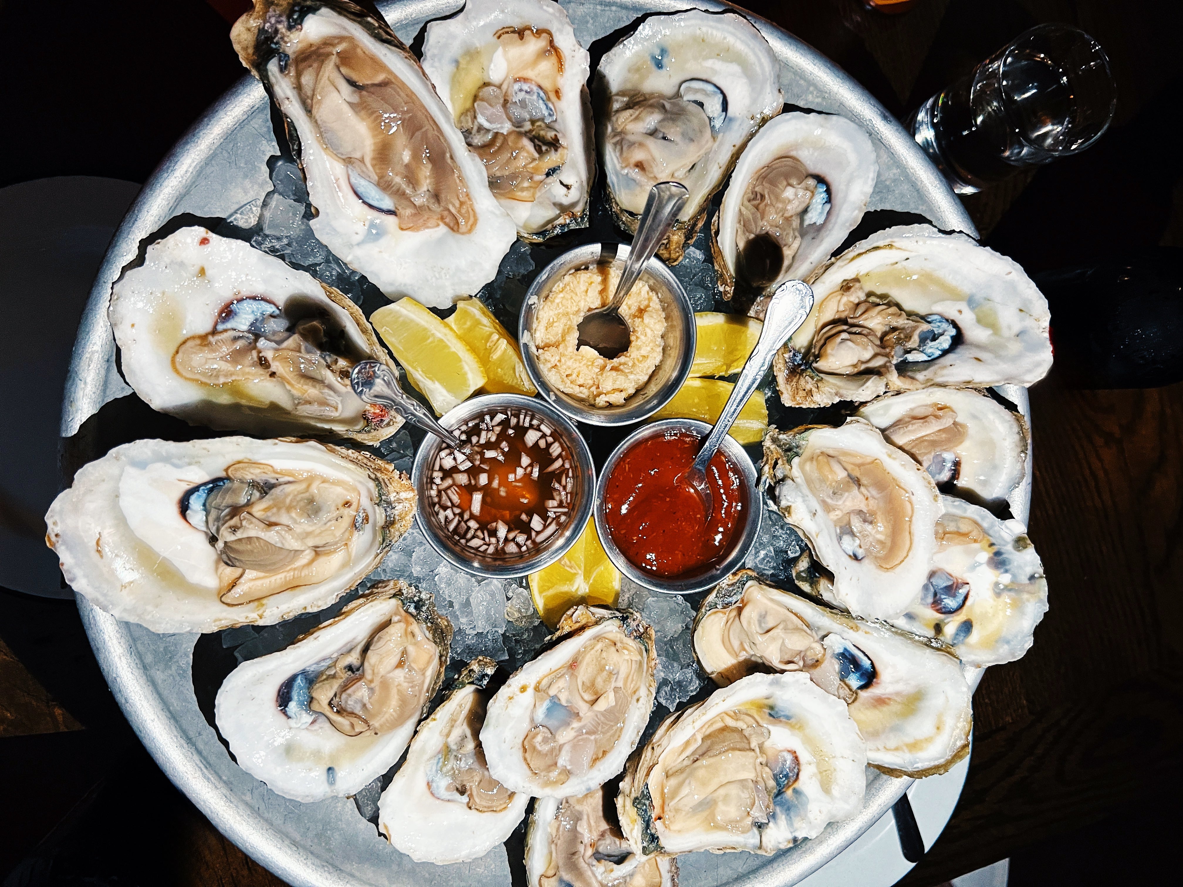 Plate of oysters on ice with lemon wedges, horseradish, cocktail sauce, and mignonette in small bowls