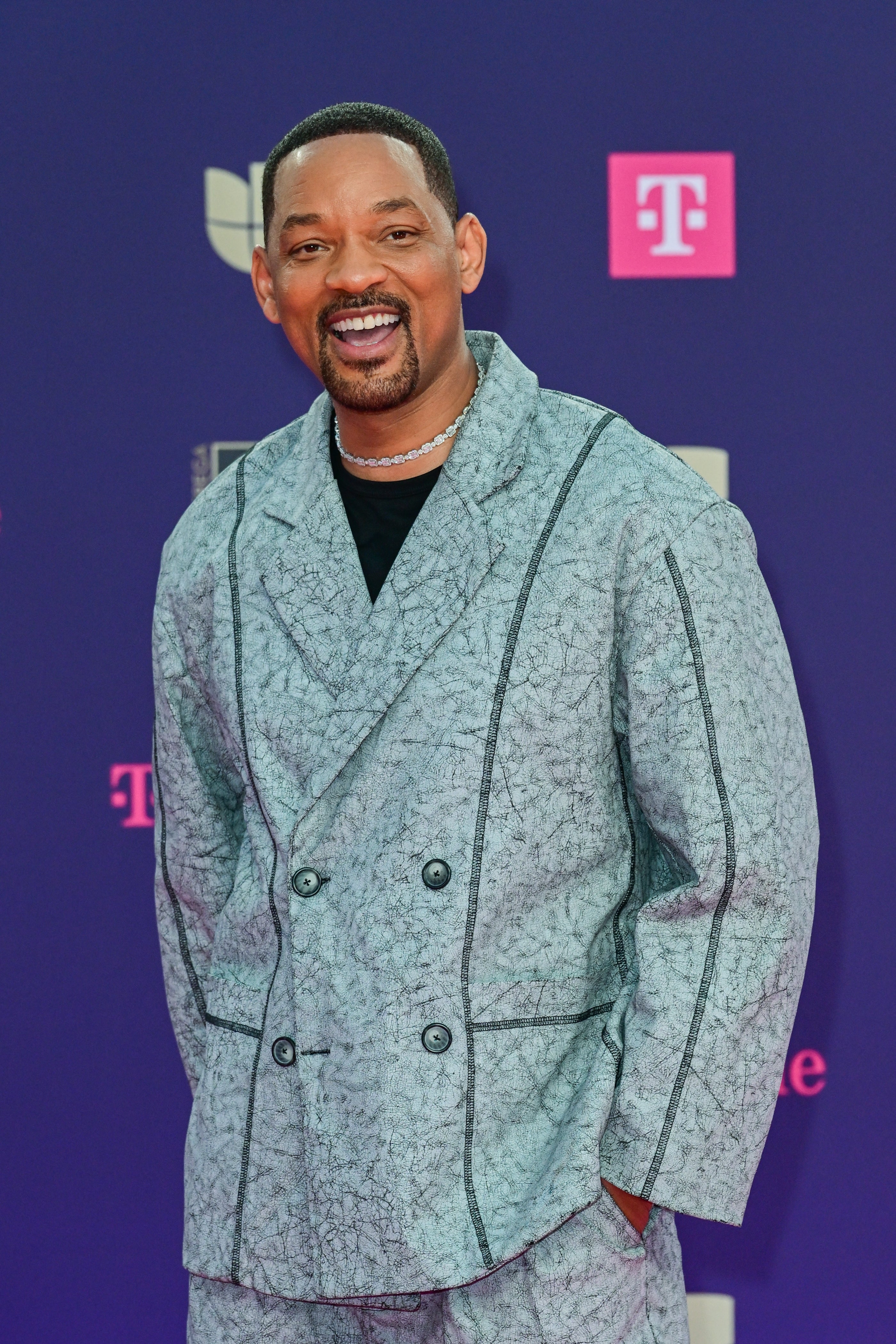 Person in patterned suit smiles on red carpet; modern, casual elegance