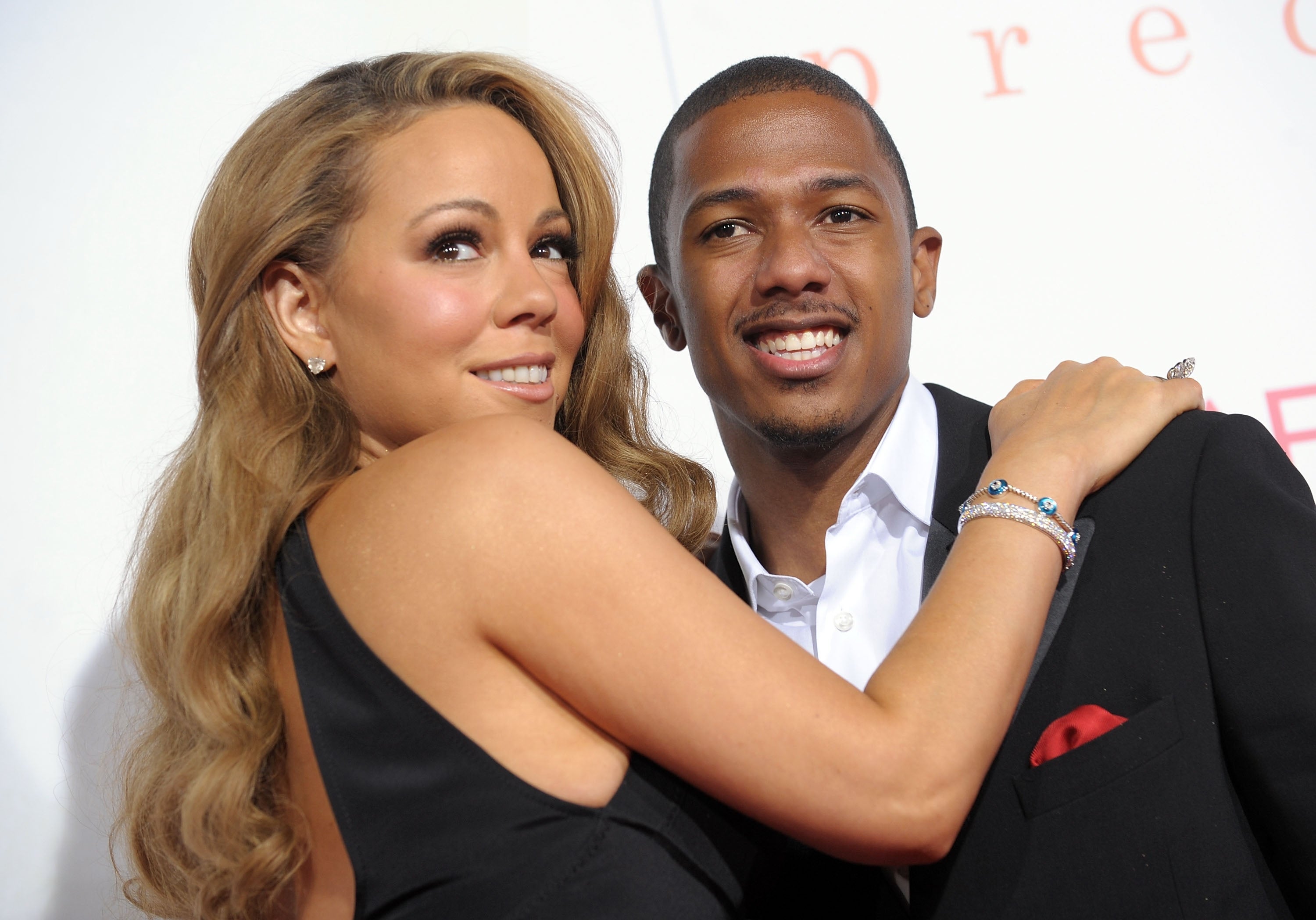 Two well-dressed individuals pose closely on a red carpet. The person on the left wears a chic dress; the person on the right is in a stylish suit