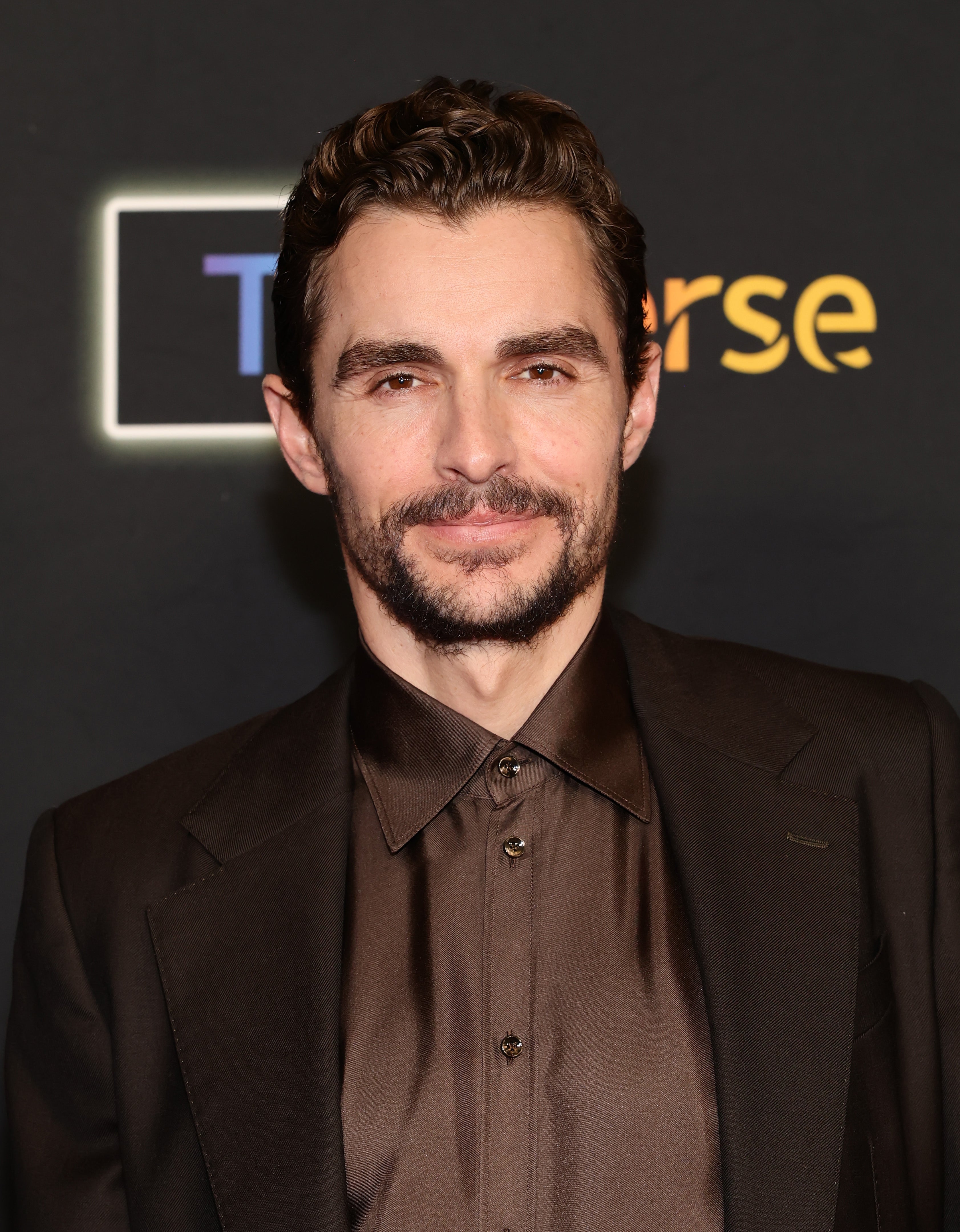 Man in a dark suit with a buttoned shirt poses at an event, smiling