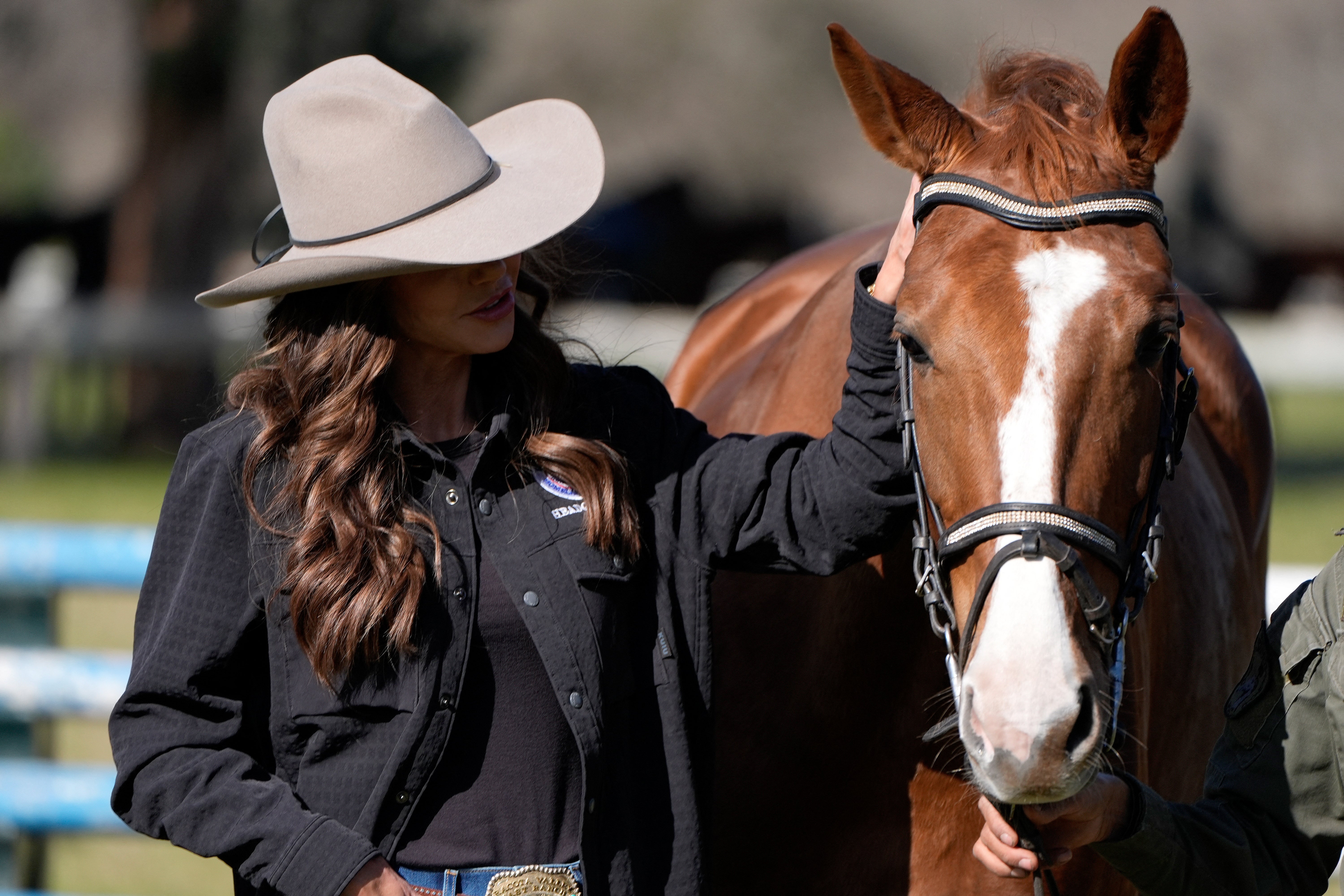 Person i vestlig stil med cowboyhatt som står ved siden av en hest og klapper forsiktig på hodet