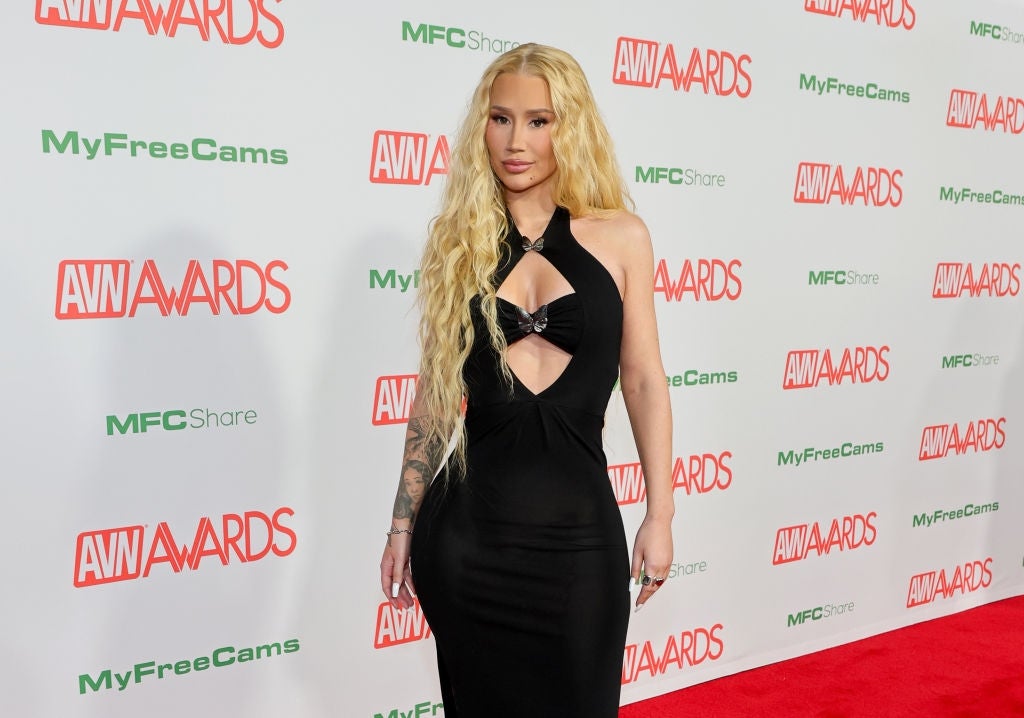 Person in a sleek black gown poses on the red carpet at an event with "AVN Awards" signage