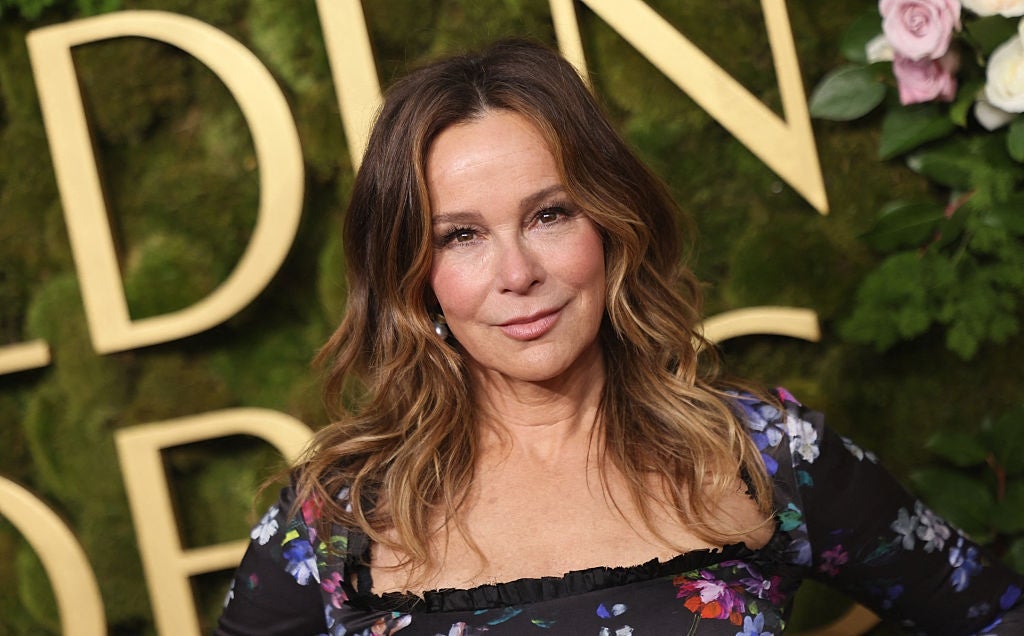 Person in floral dress poses at an event with a greenery backdrop decorated with flowers