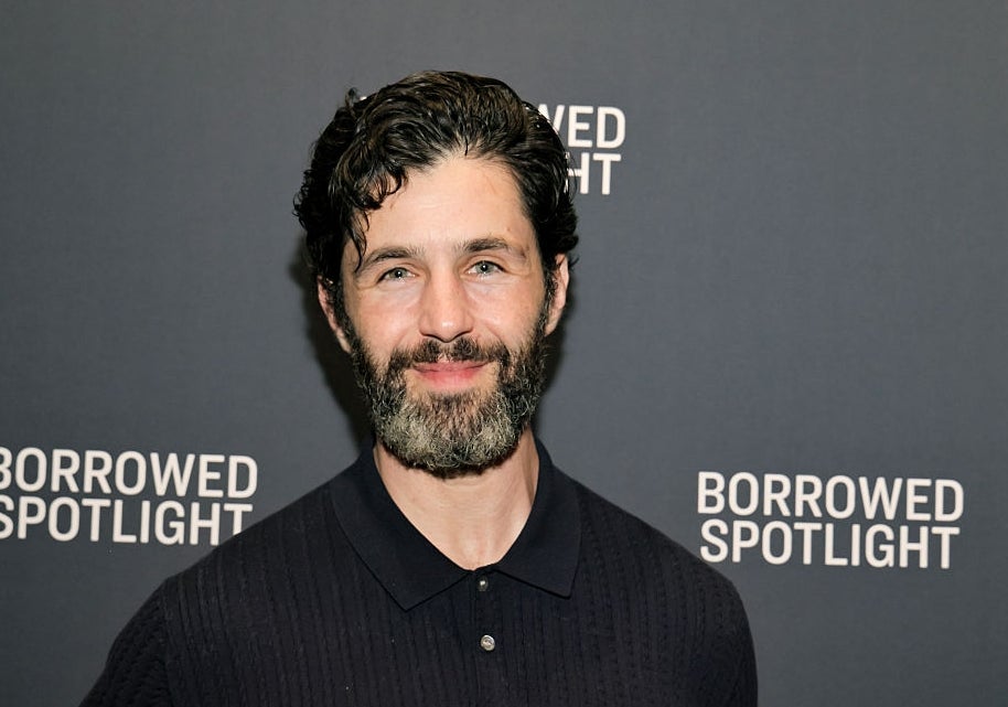 Man with a beard smiles in front of a "Borrowed Spotlight" backdrop, wearing a dark, textured shirt