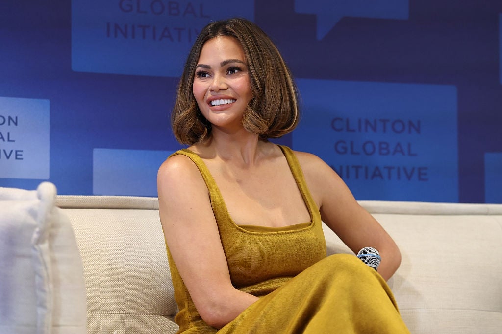 Person seated on a panel, wearing a sleeveless, elegant dress, smiling at an event with a Clinton Global Initiative backdrop