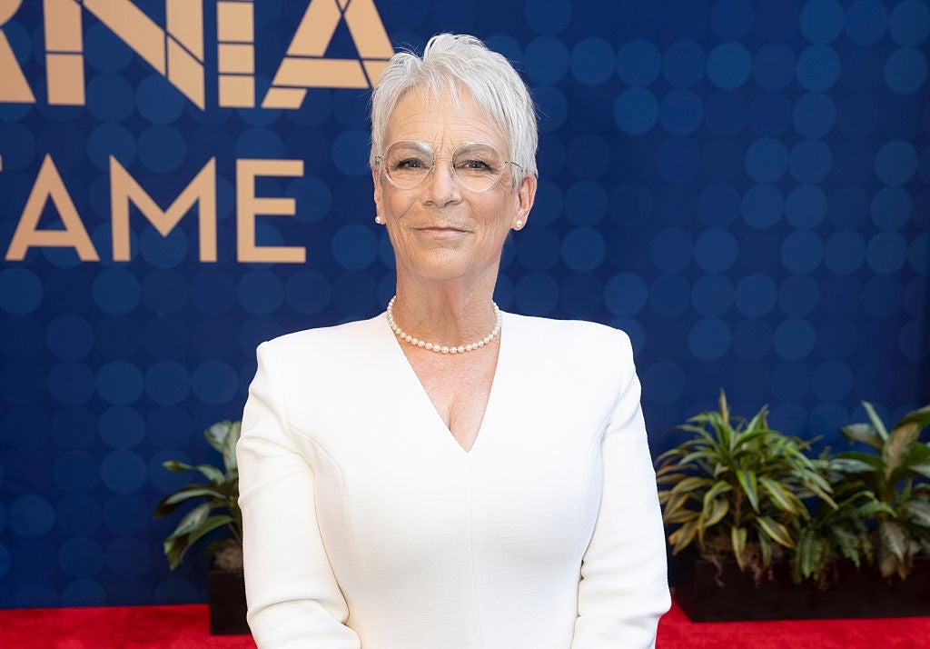 Person in elegant, white, long-sleeved outfit on a red carpet with a blue background