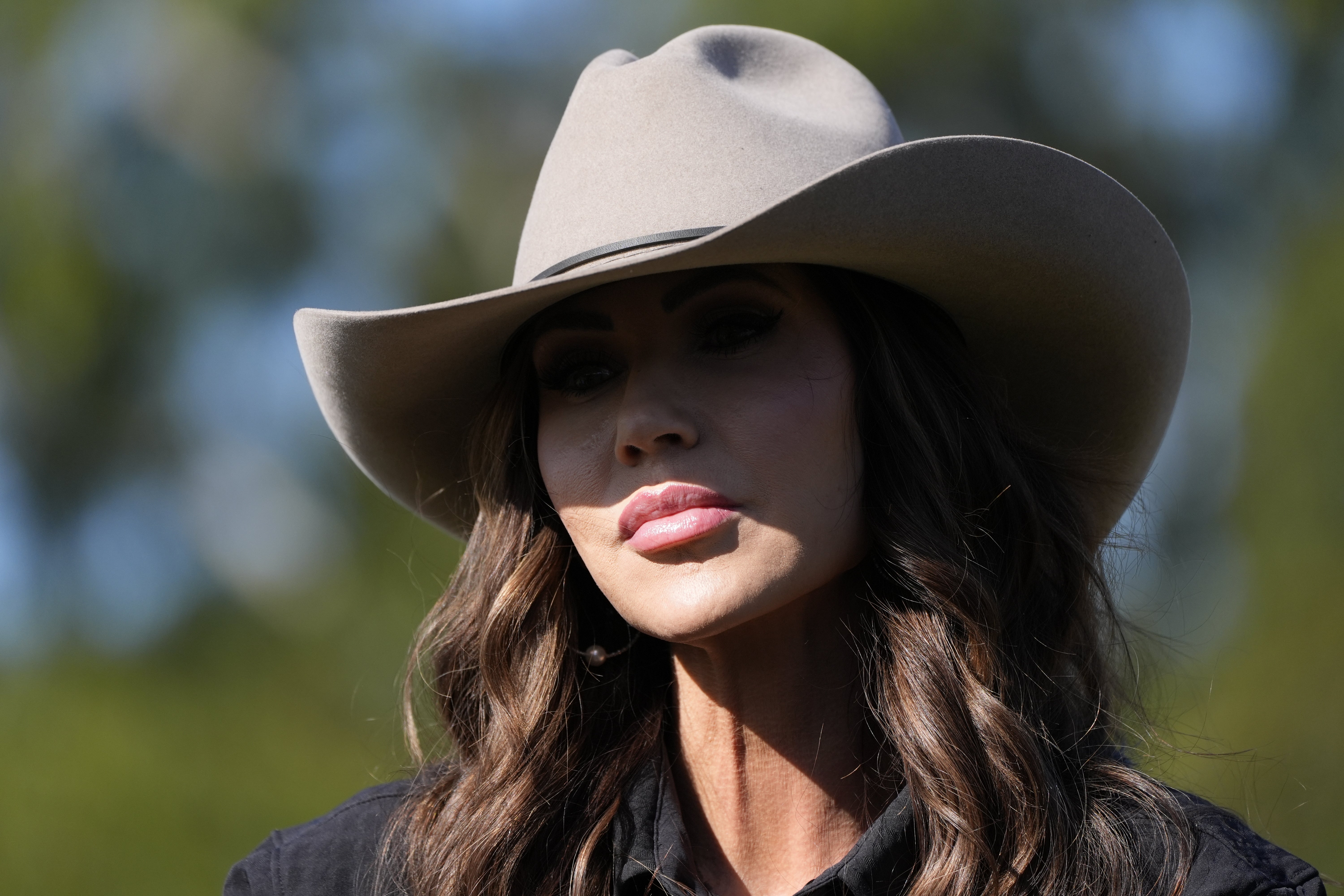 Person som har på seg en cowboyhatt med langt hår synlig, står utendørs